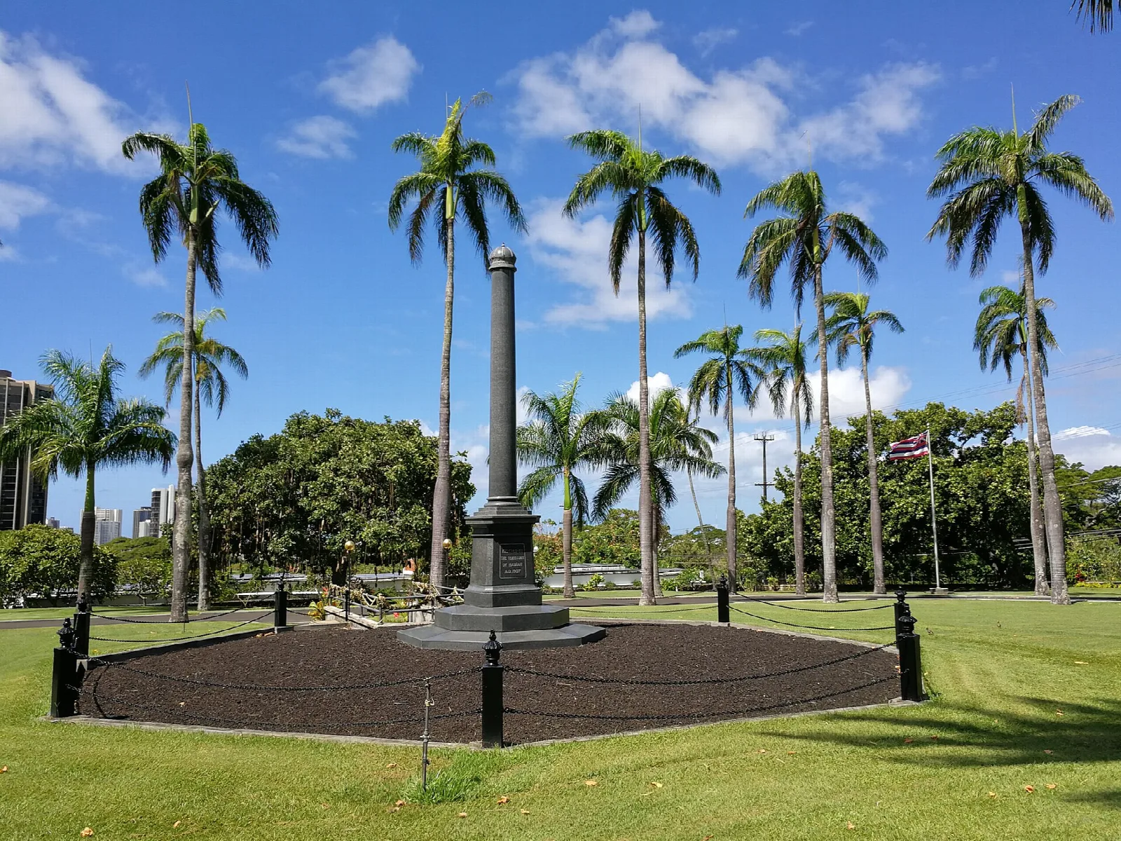 A dark monument in a ring of soil among tall palms