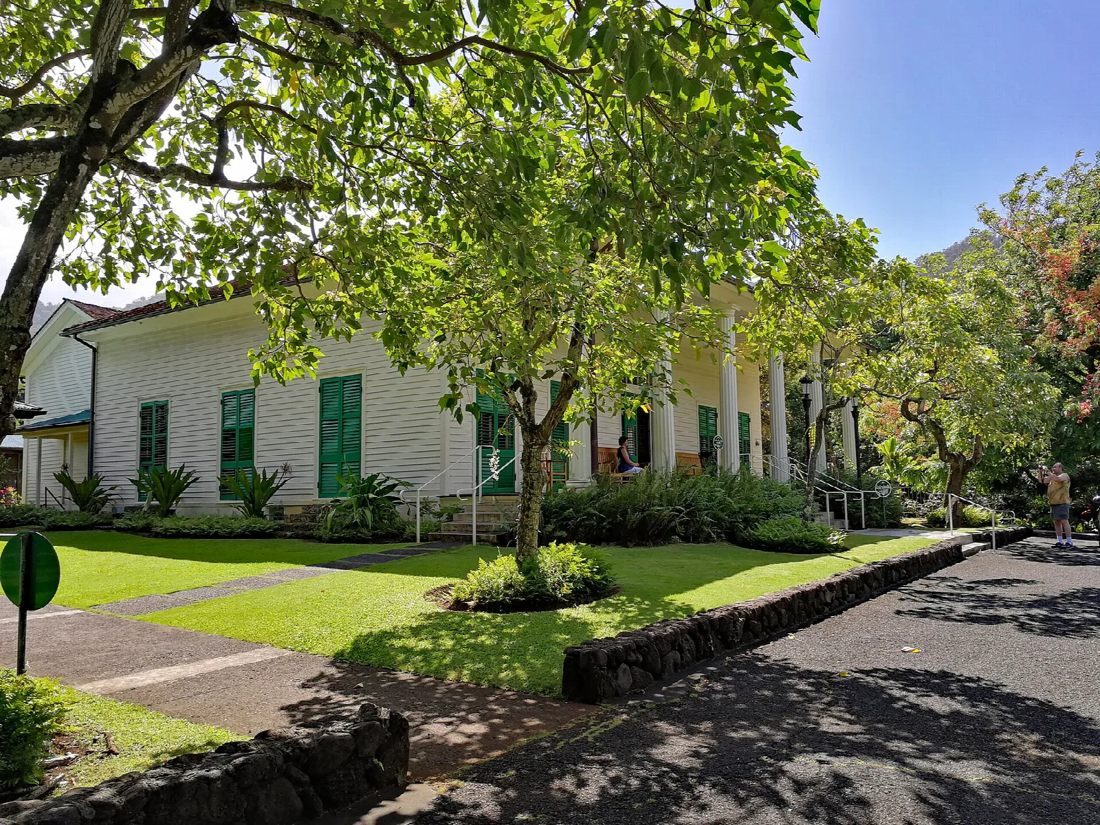 A white house with a porch seen through trees along a path