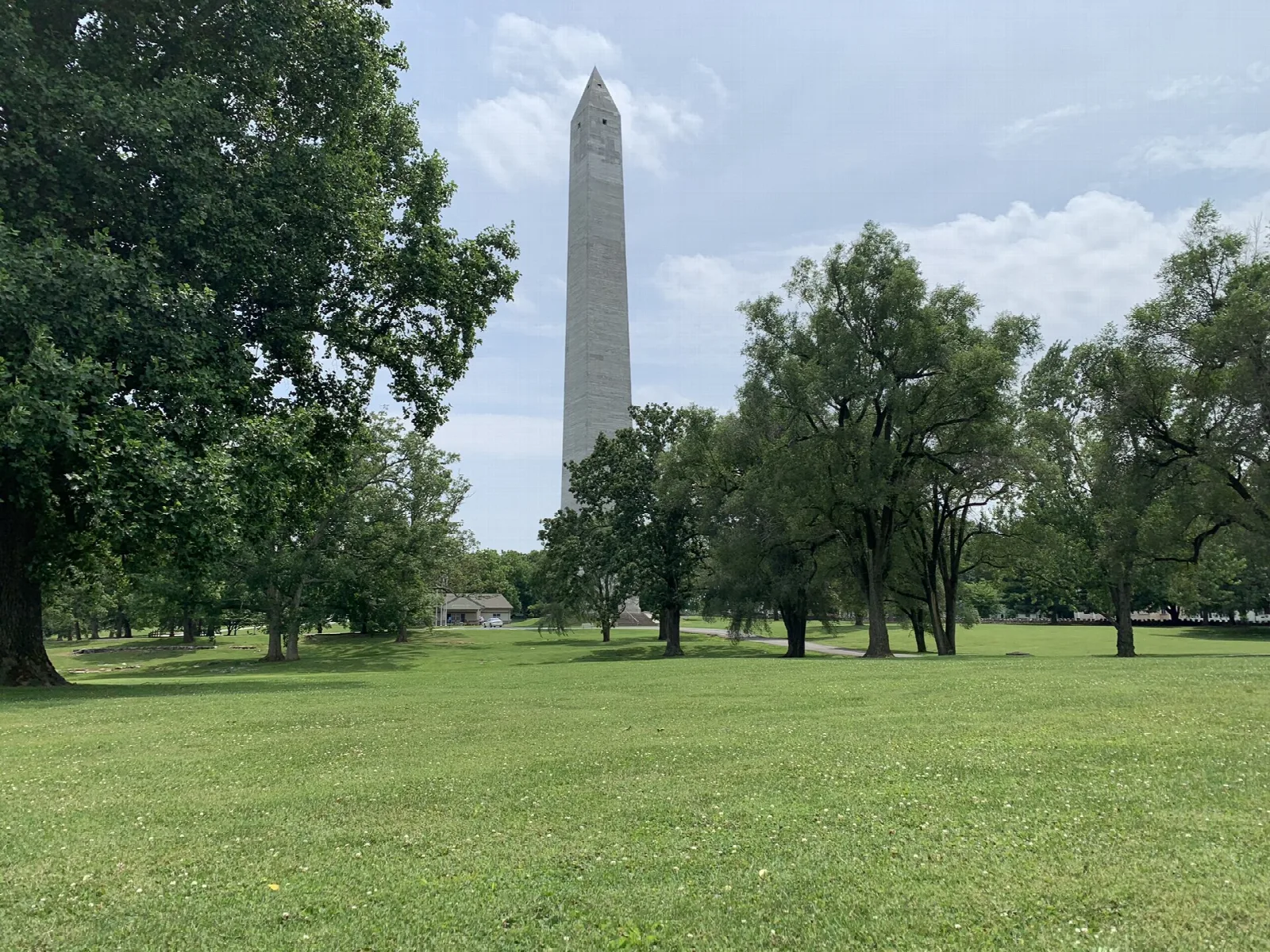 Tall stone obelisk rising above a wide grassy lawn and large trees