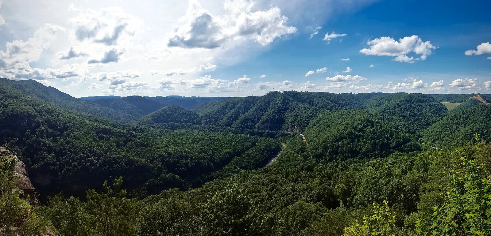 Wide view over forested ridges and valleys under a blue sky with clouds