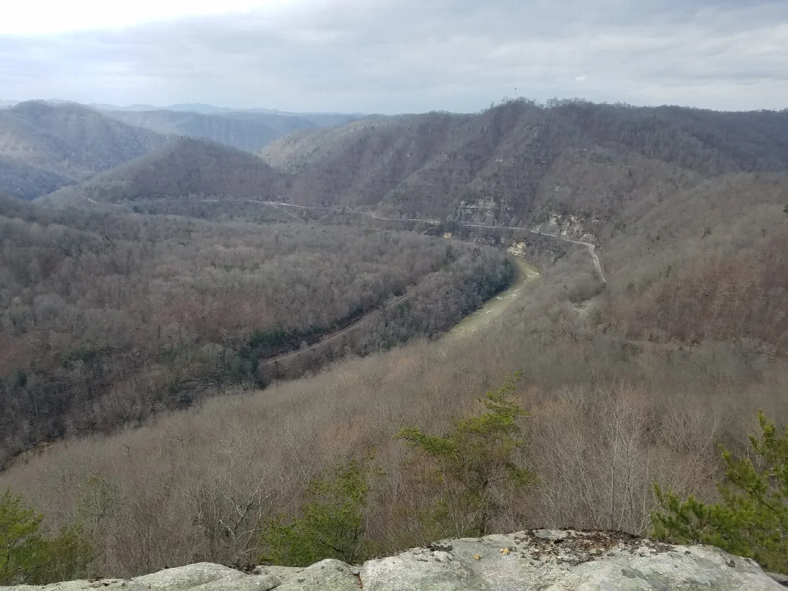 Bare late-winter ridges and a river bend seen from a rock ledge