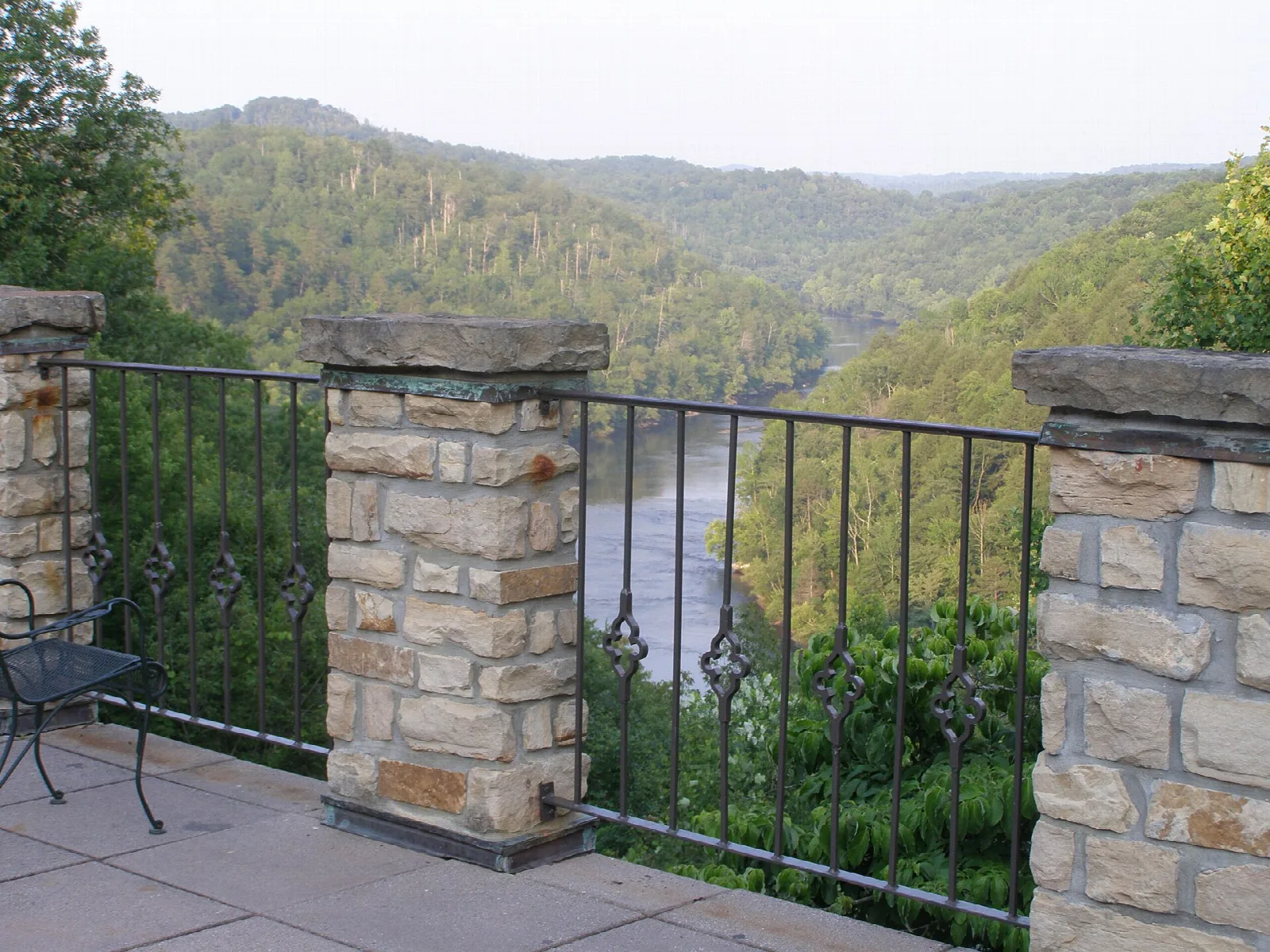 Stone and iron terrace railing overlooking a forested river valley