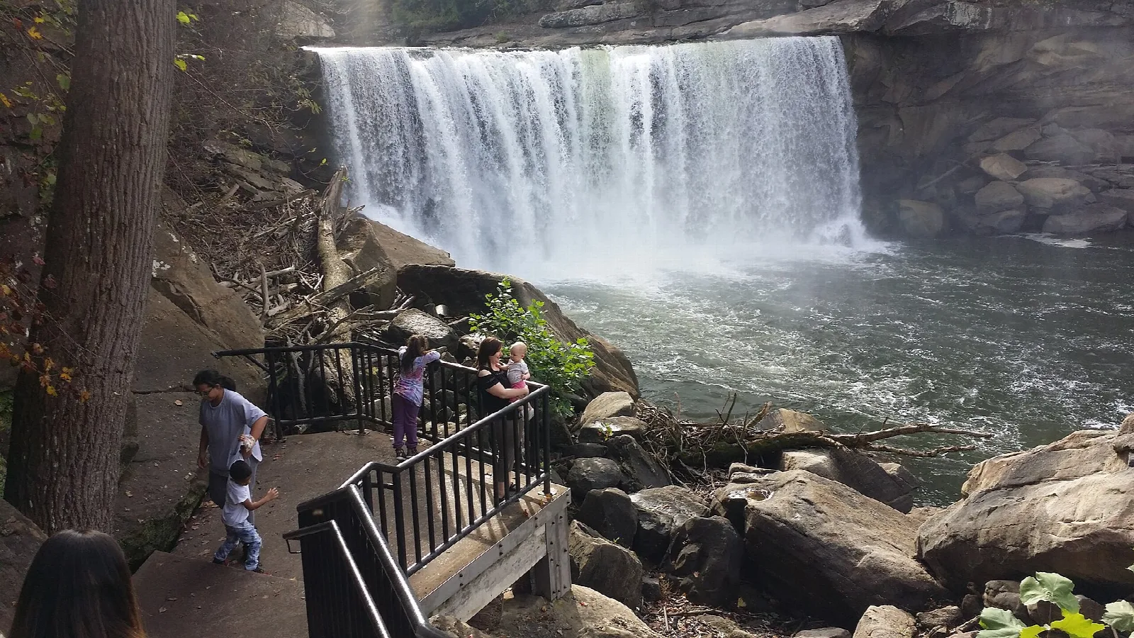 Visitors on a wooden walkway above a waterfall and boulders
