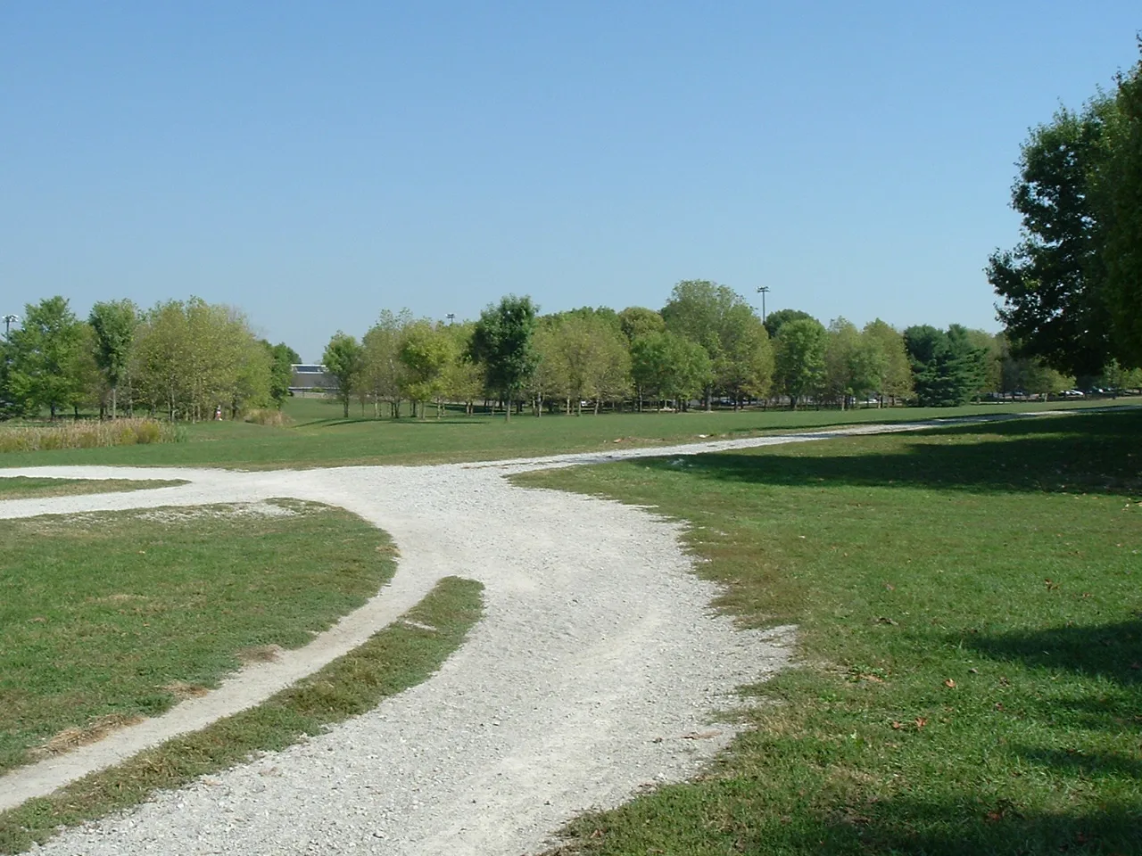 Gravel path curving through mown grass with trees in the distance under a clear sky