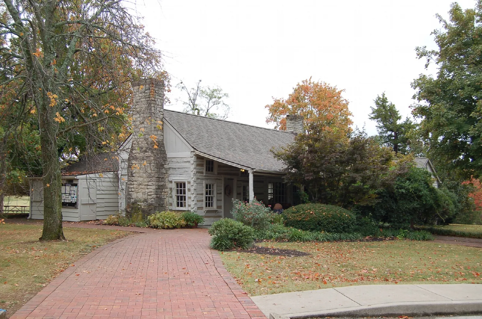 Log and stone house beside a brick path with autumn trees