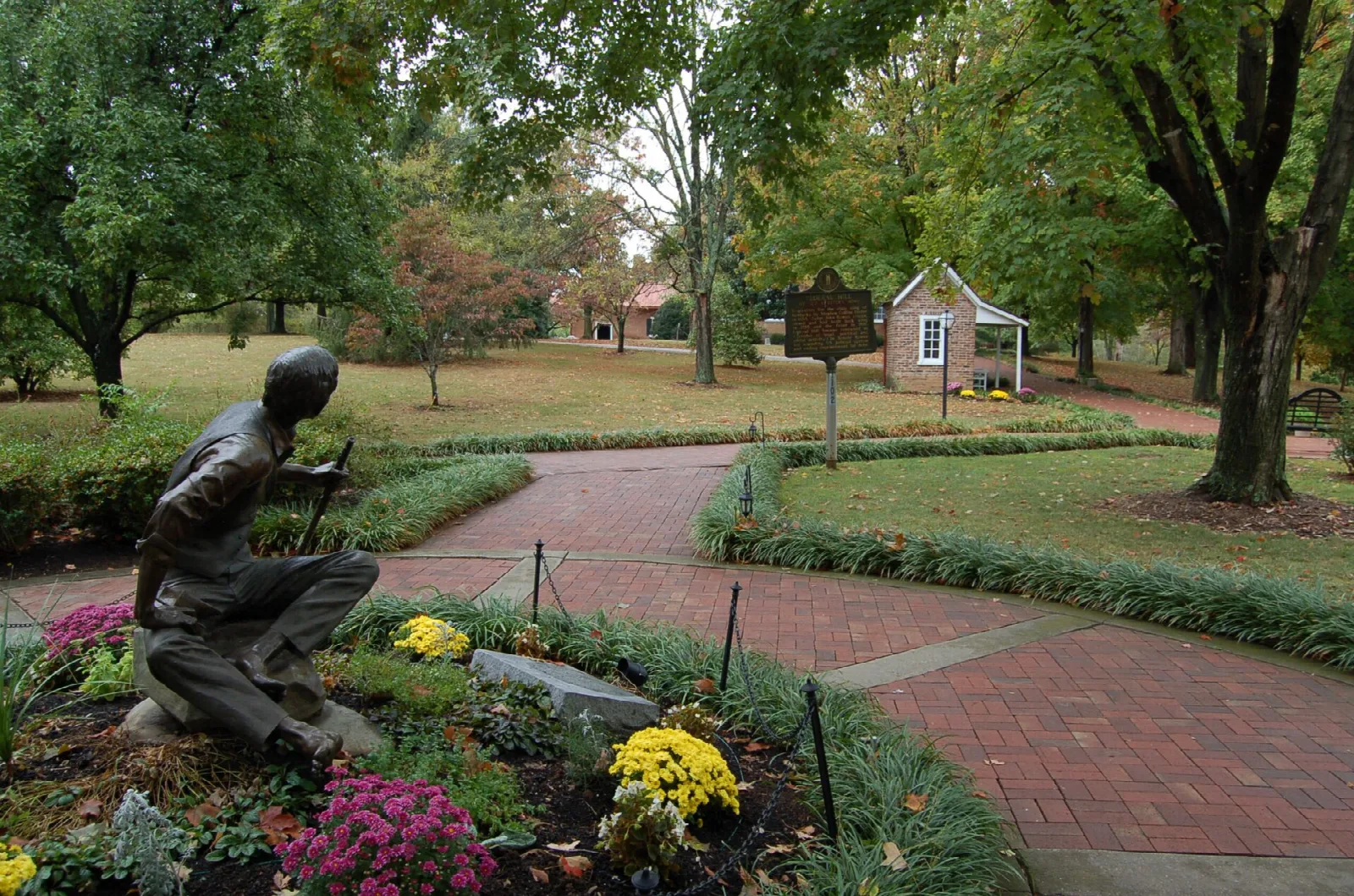 Bronze statue of a seated young man in a flower bed beside a brick path