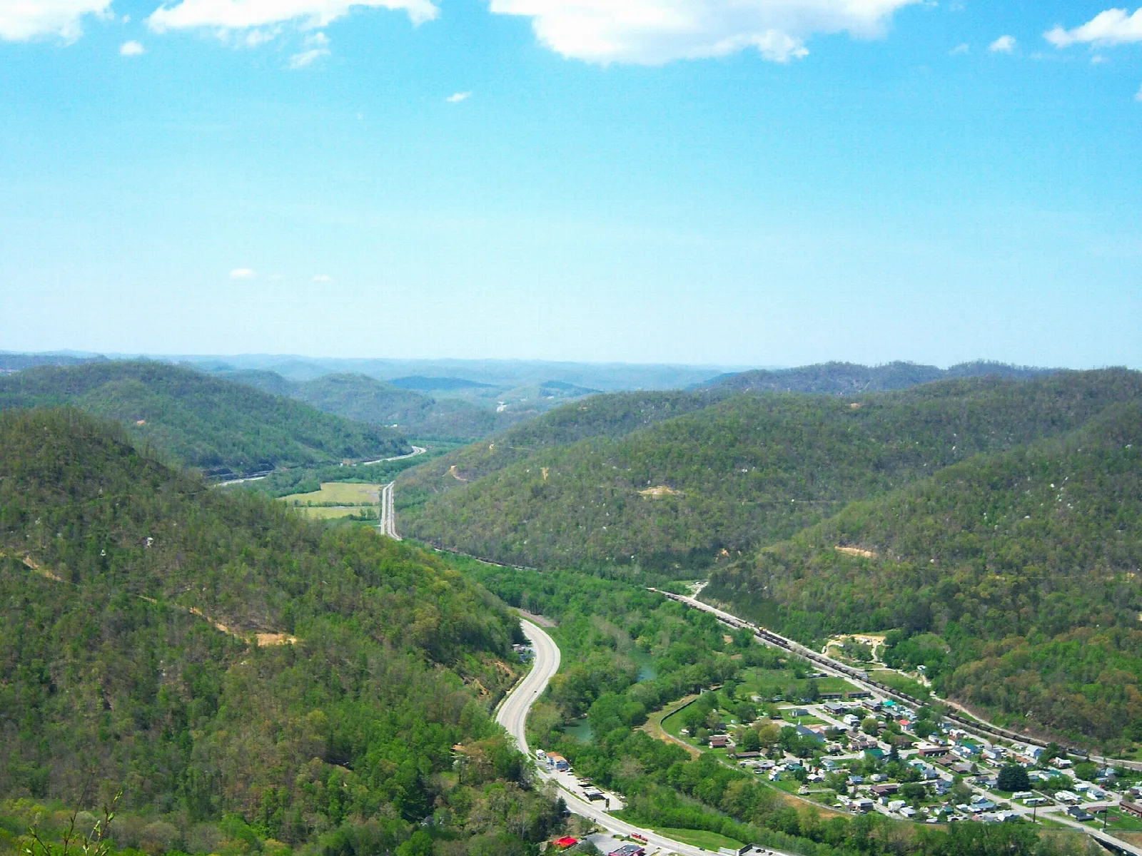 Wide view over forested mountains and a valley with a road and town below