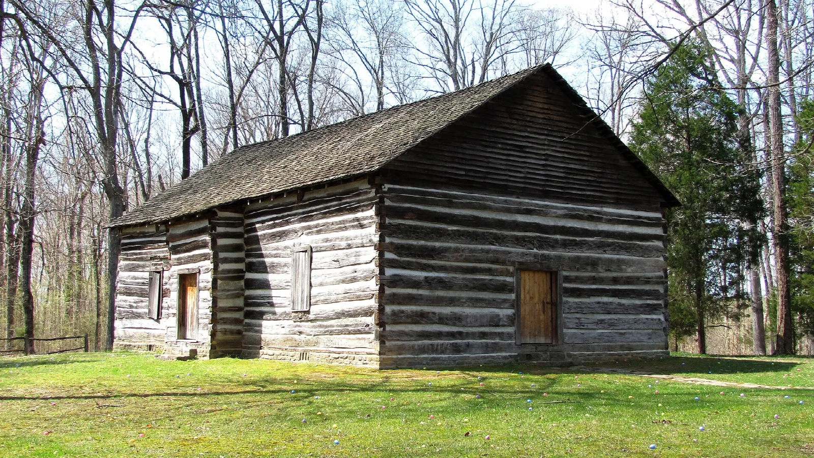 Old log meetinghouse with a dark roof on a green lawn among bare spring trees