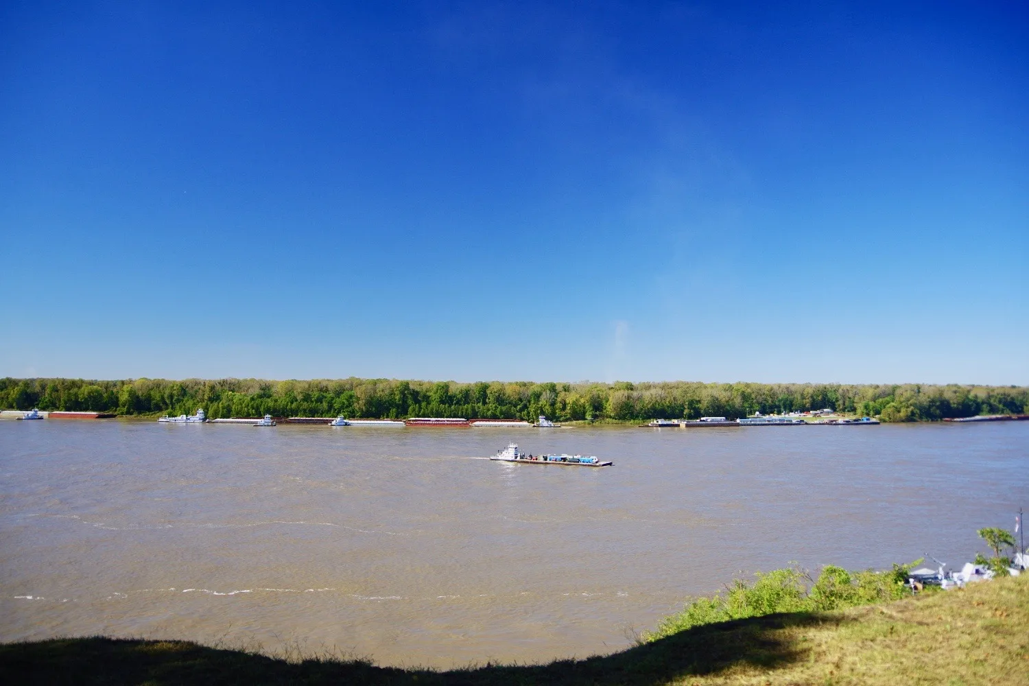 Broad river with a barge and a distant tree line under a deep blue sky