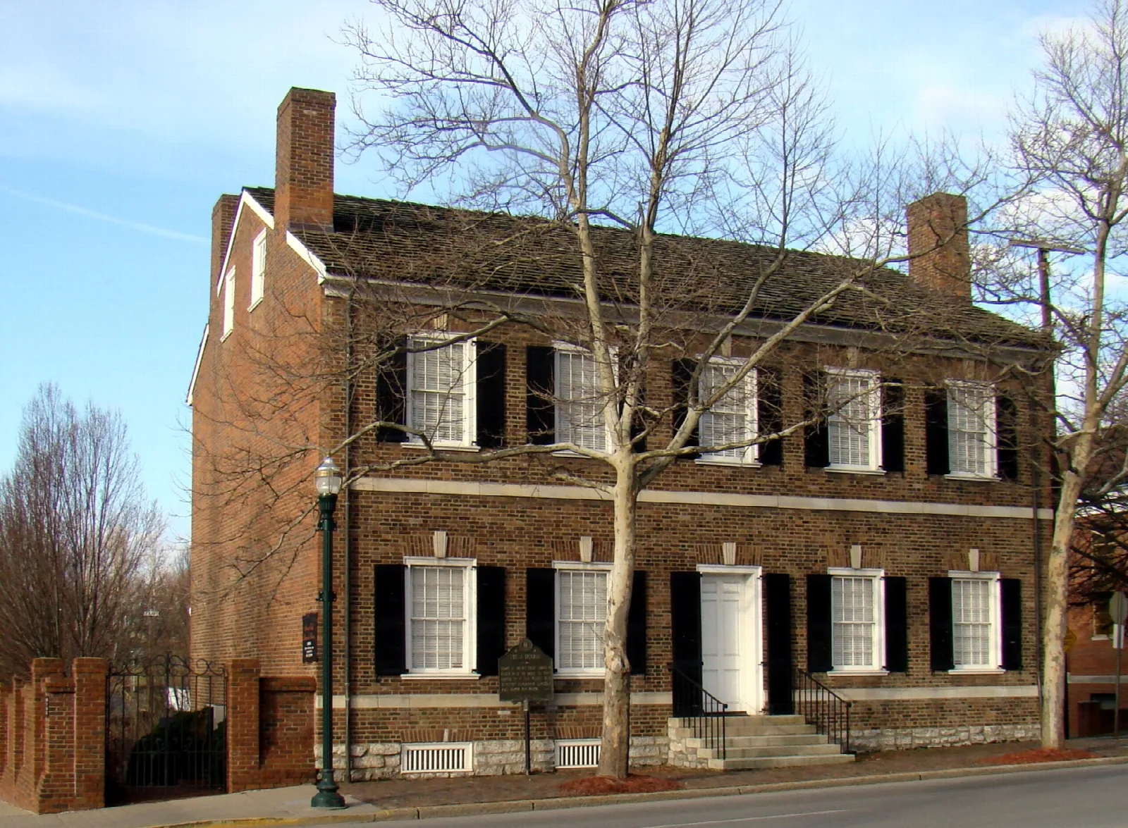 Brick house with black shutters seen from the corner under a blue sky