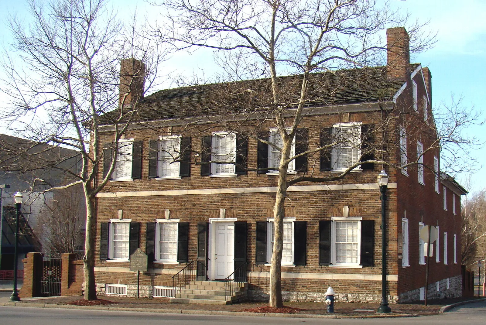 Two-story brick house with black shutters and bare trees on a corner street