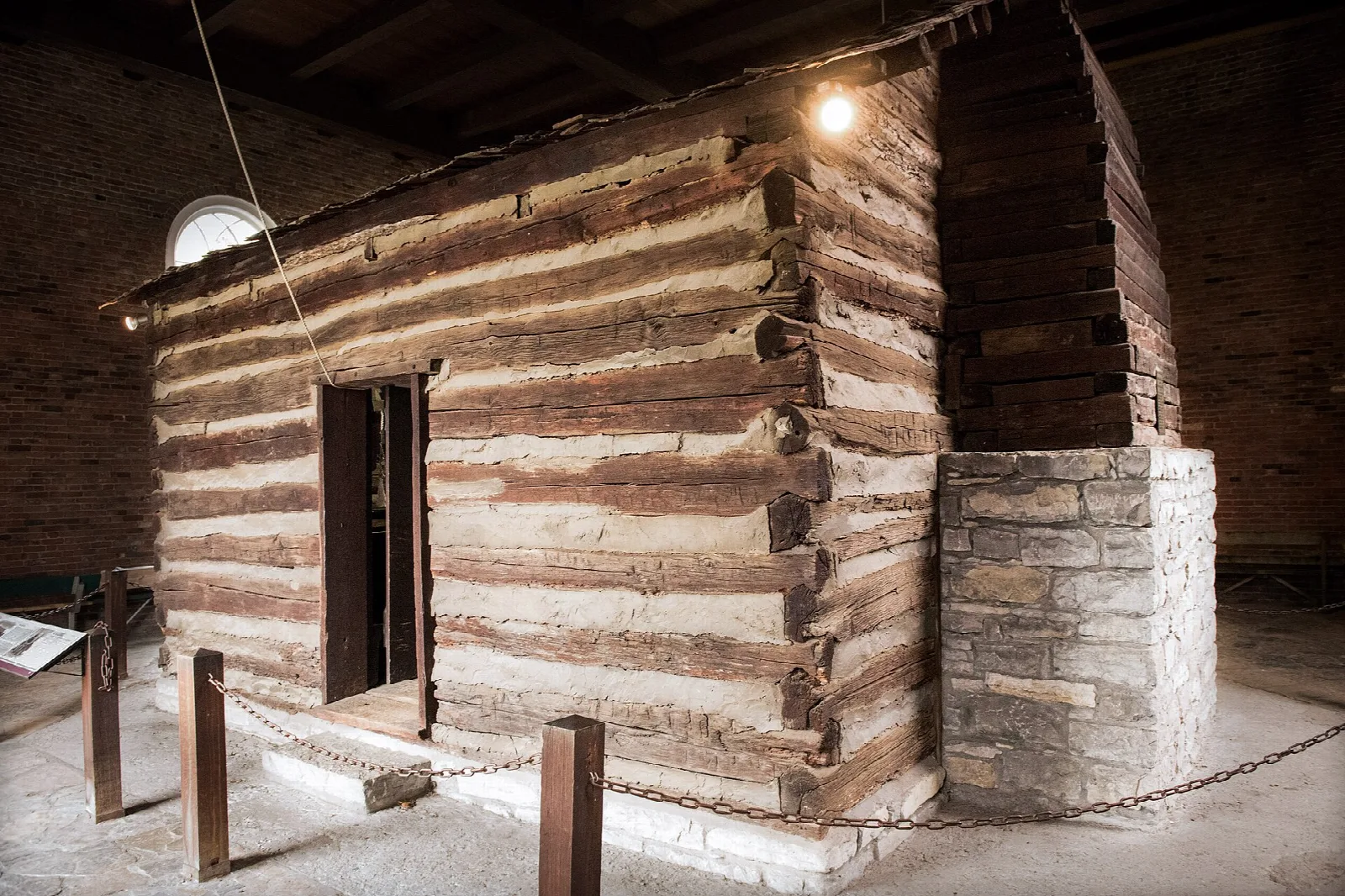 Old log cabin inside a protective stone structure, lit from above