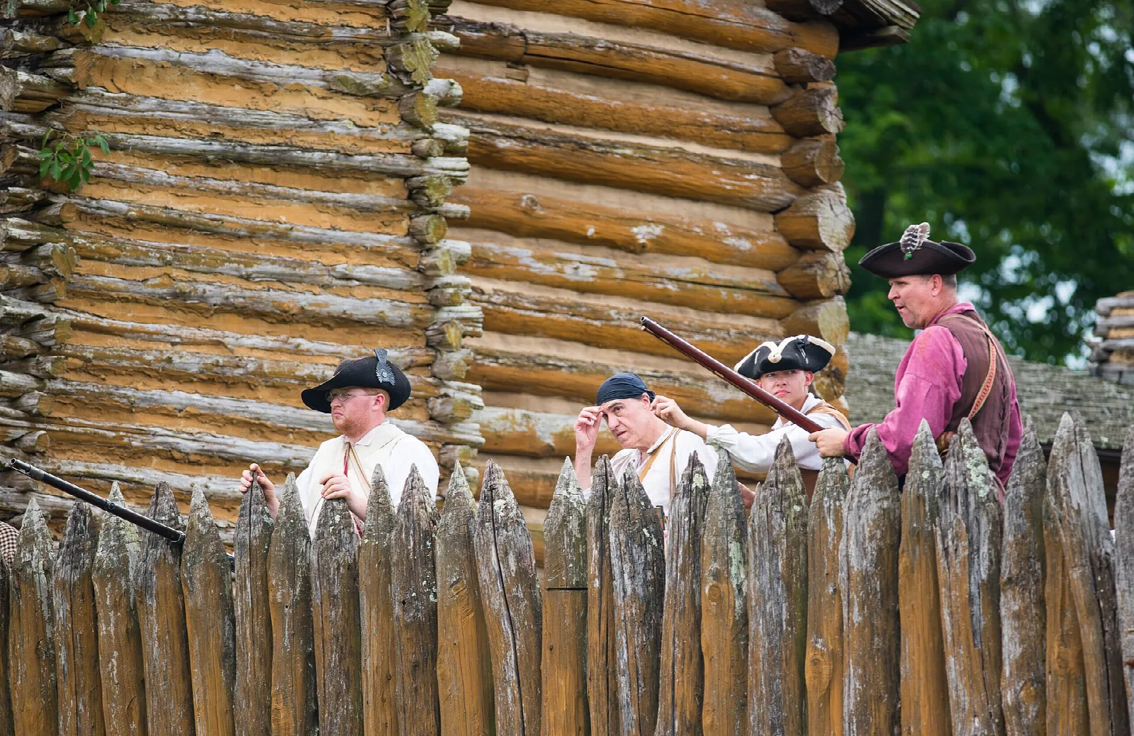 Costumed reenactors behind the sharpened log stockade wall