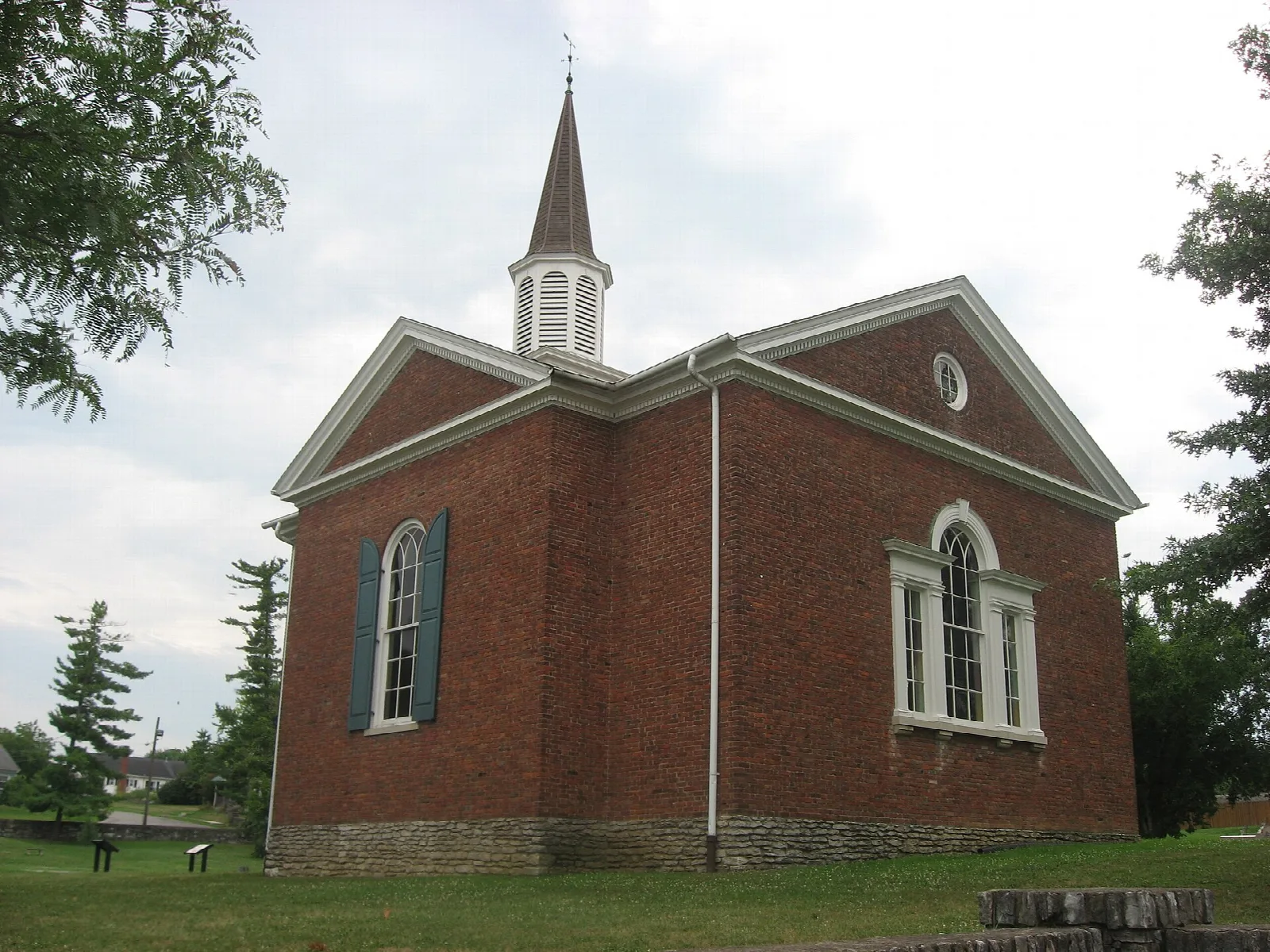Brick temple with a white steeple and arched windows on a green lawn