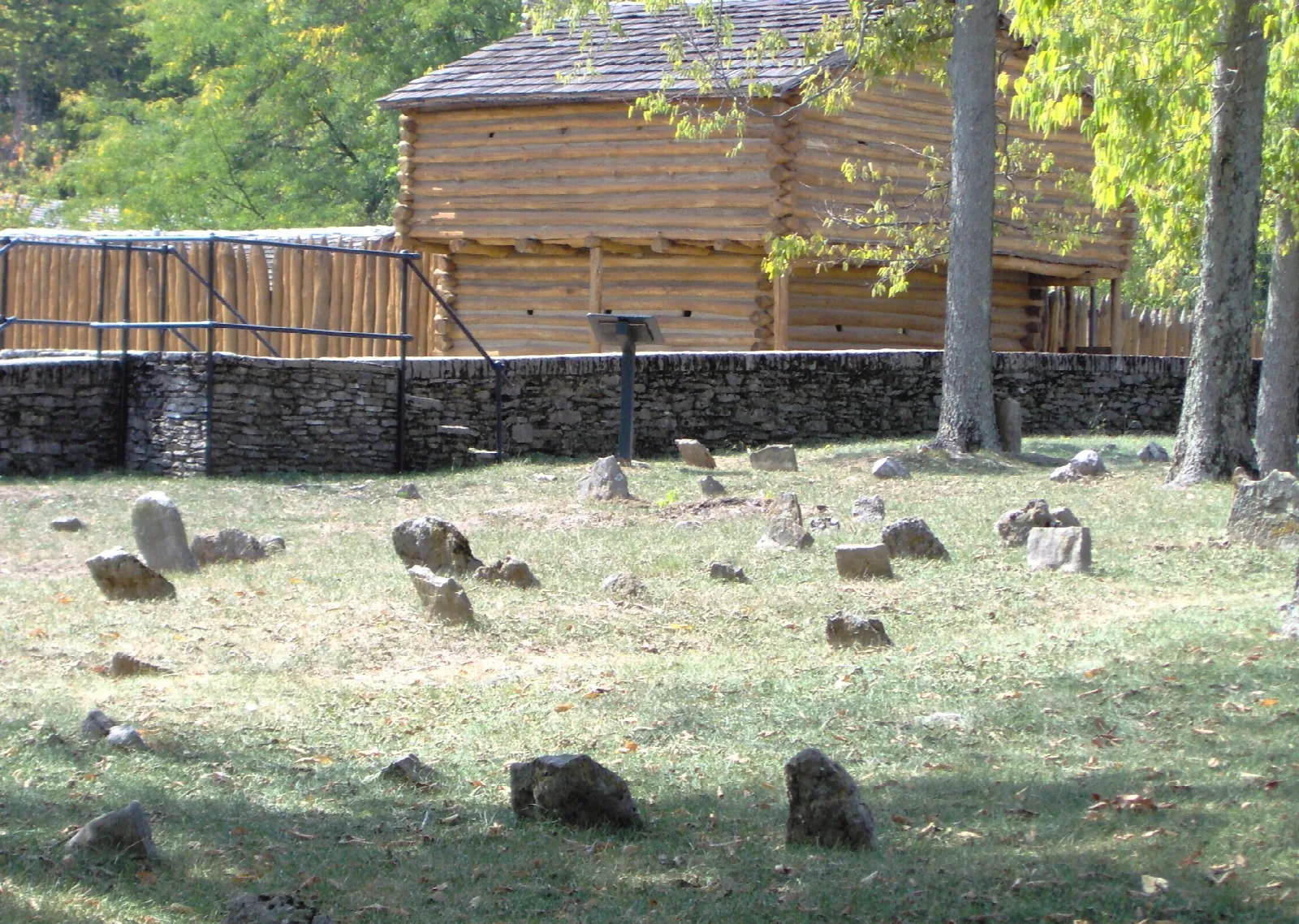 Old gravestones in grass with the fort's log walls behind