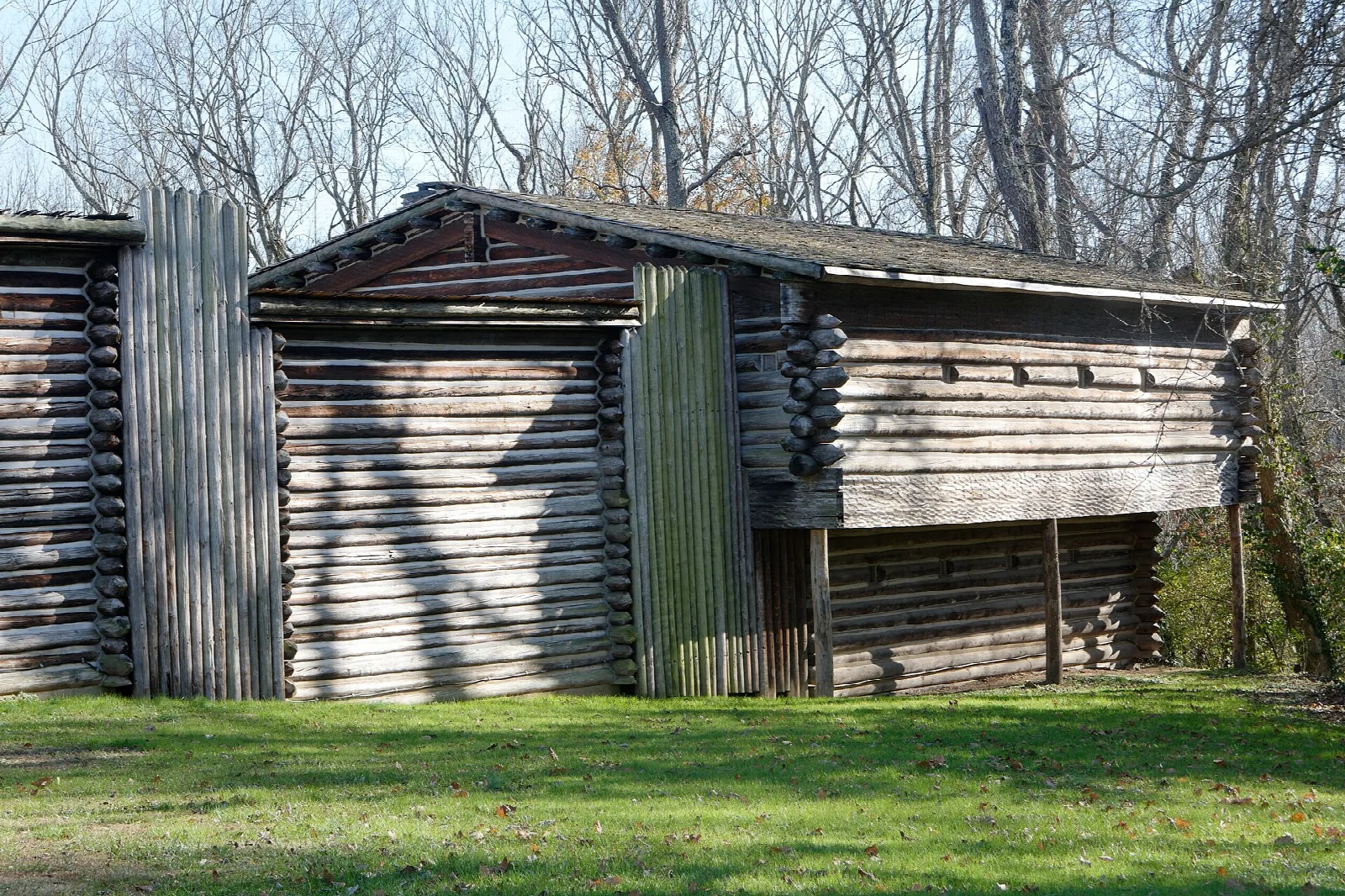 Log blockhouse with a plank gate and wooden stockade on a green lawn
