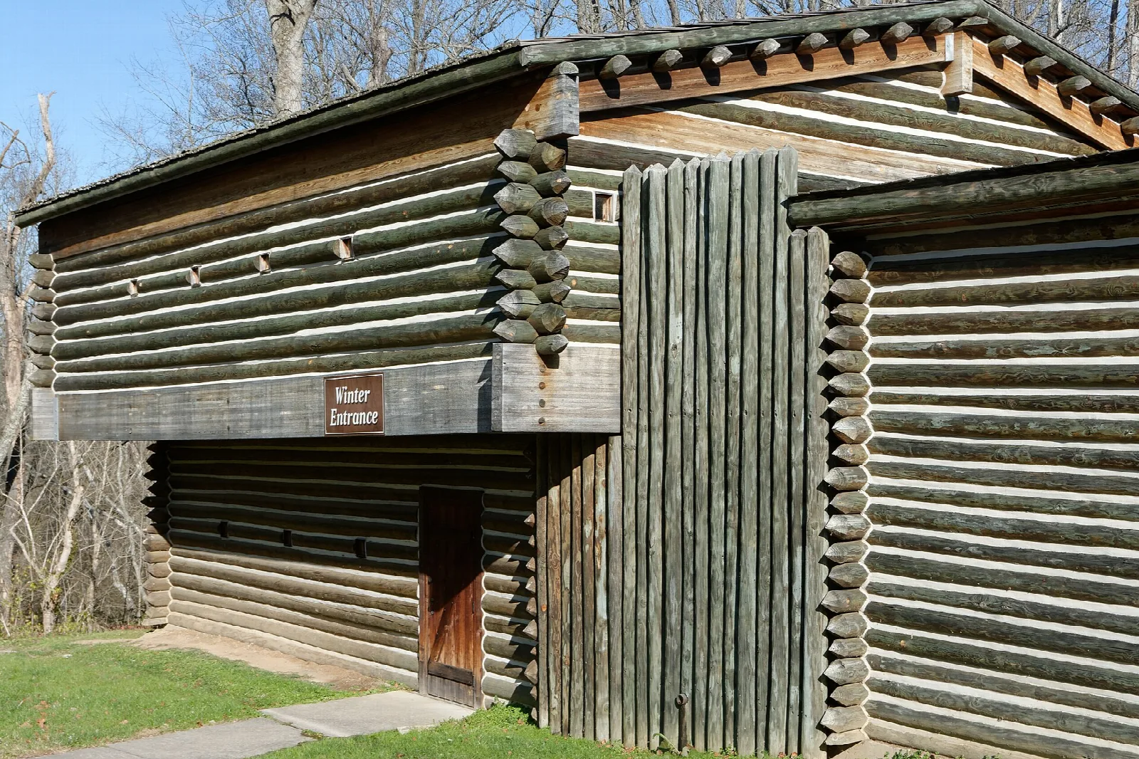 Two-story log blockhouse with a sign beside a stockade gate