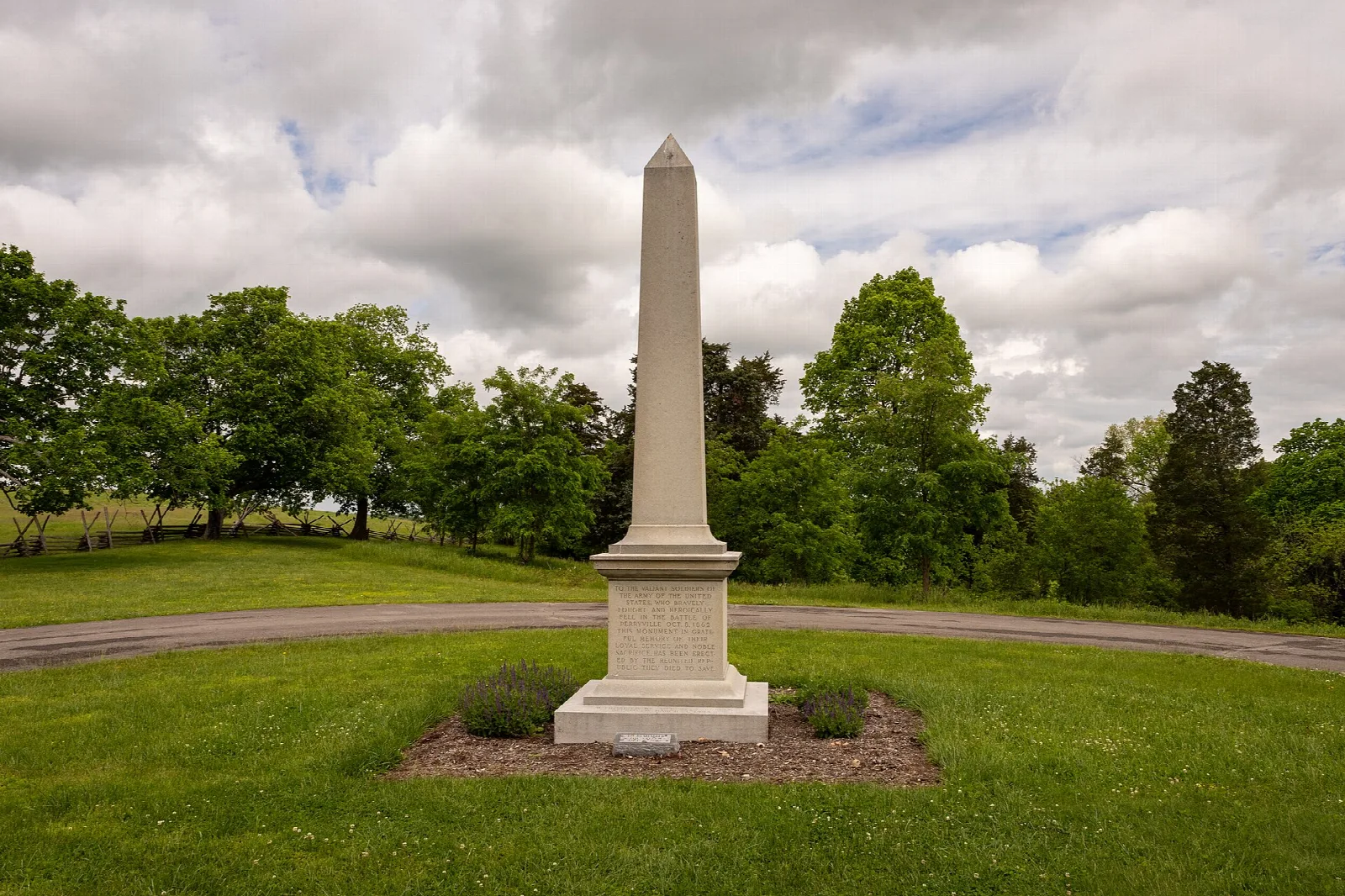 Stone obelisk monument on a lawn ringed by trees