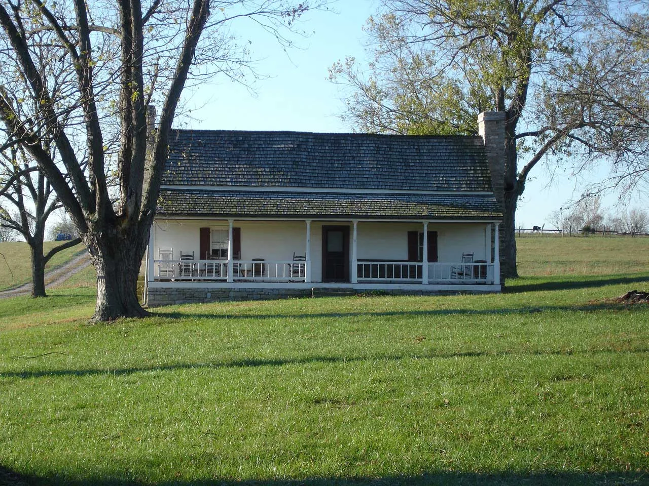 Small white farmhouse with a porch and bare trees on open grass