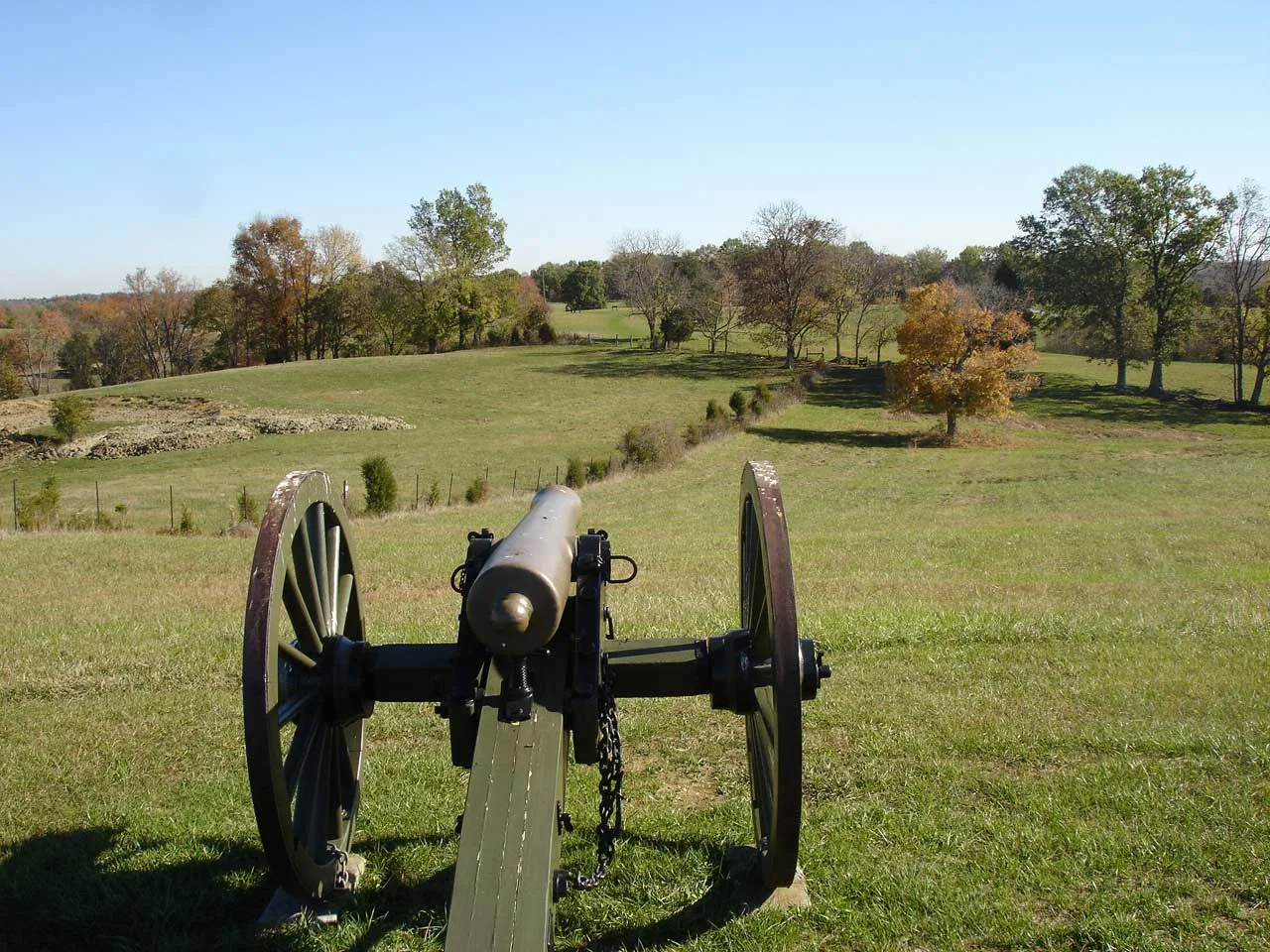 Civil War cannon on a grassy rise with open farmland and trees beyond