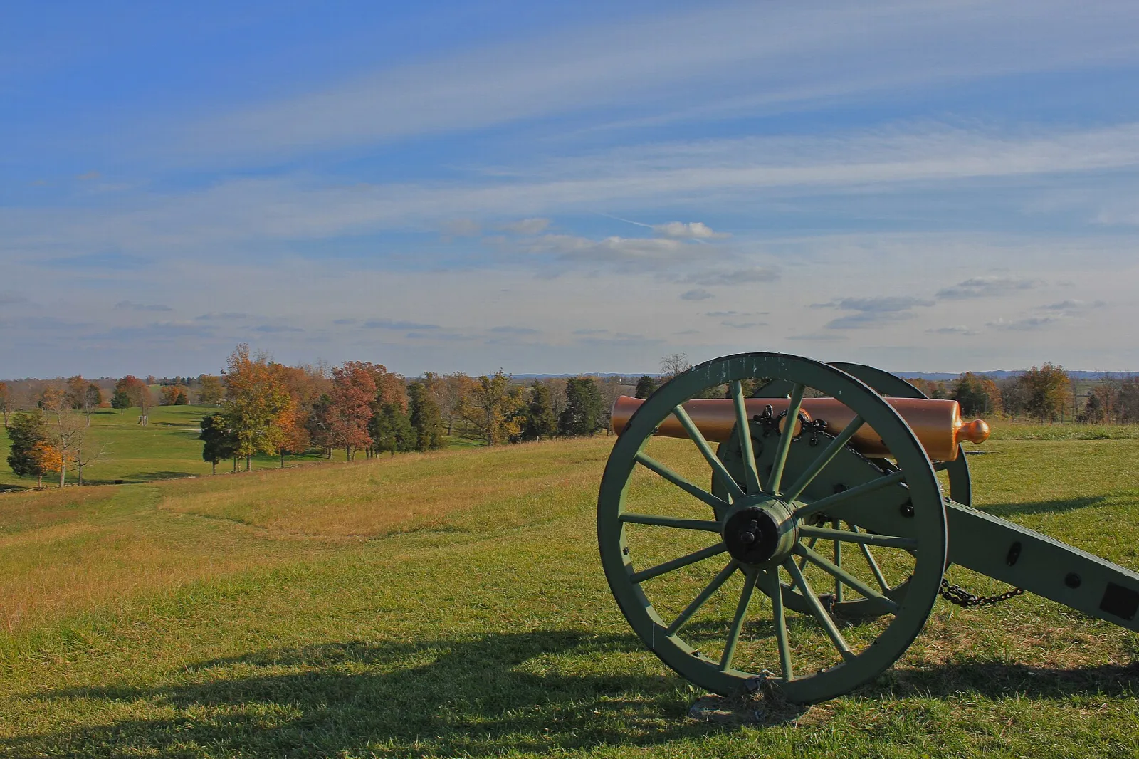 Cannon wheel on a grassy hill under a blue sky with autumn trees in the distance