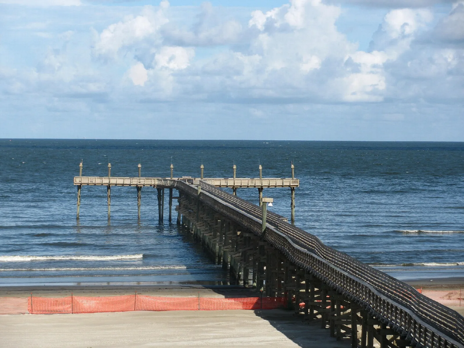 Long wooden fishing pier running out into the blue Gulf of Mexico under a partly cloudy sky