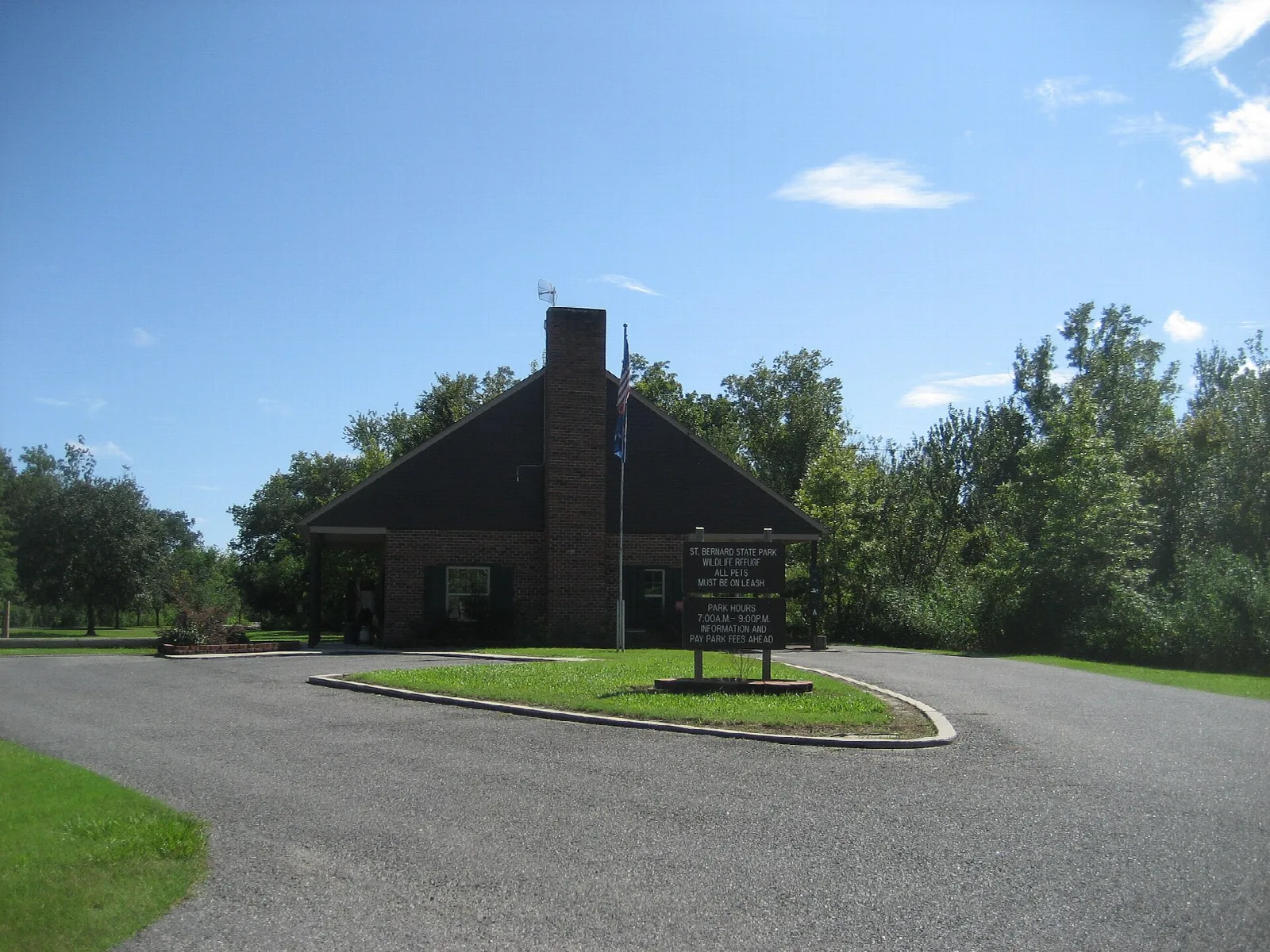 Brick building with a tall chimney and a sign, beside a curved paved drive and green trees