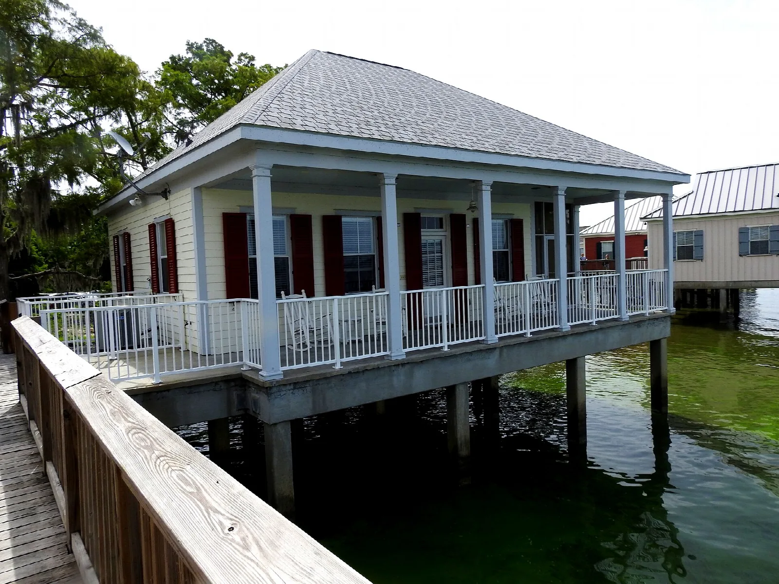 Raised cabin with a covered porch on stilts over green lake water