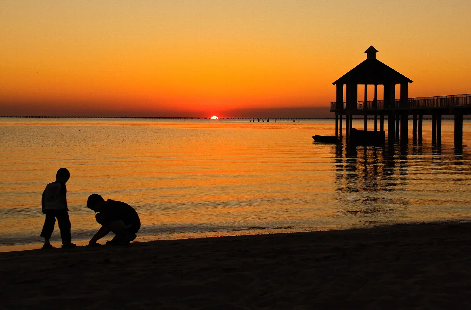Gazebo on a pier silhouetted against an orange sunset over the lake