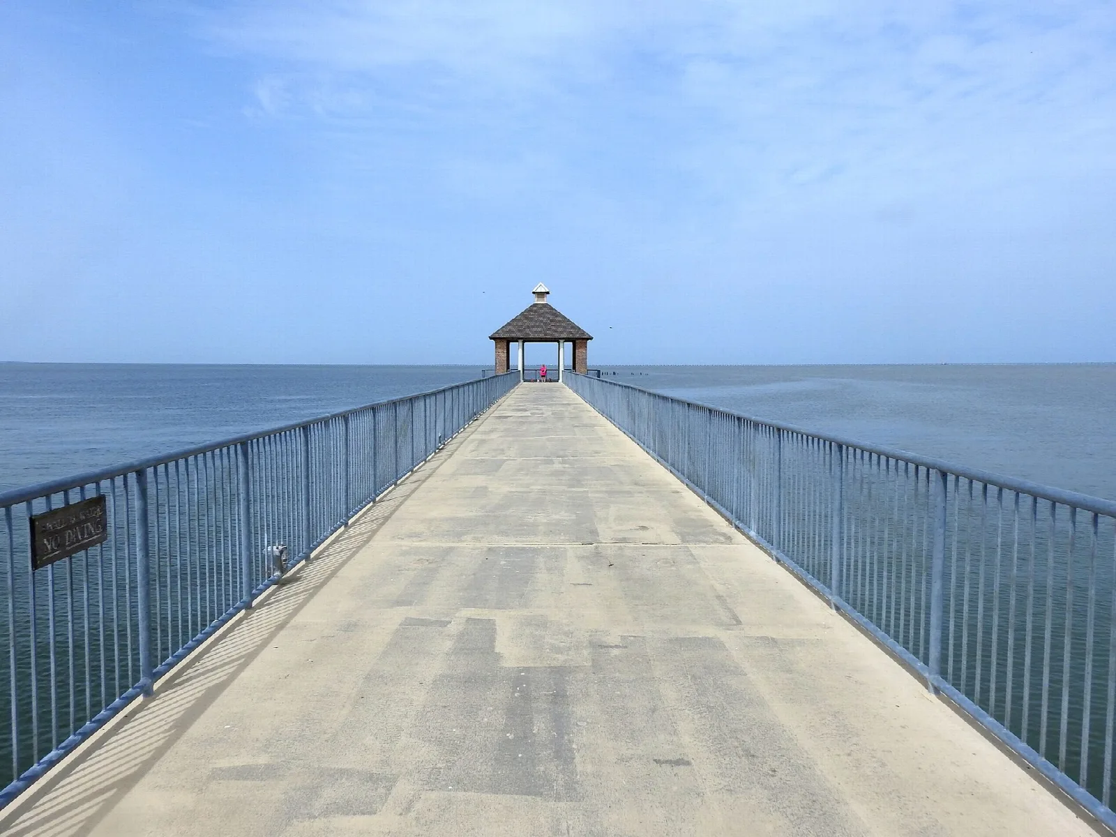 Concrete fishing pier with blue railings running out to a small gazebo over Lake Pontchartrain