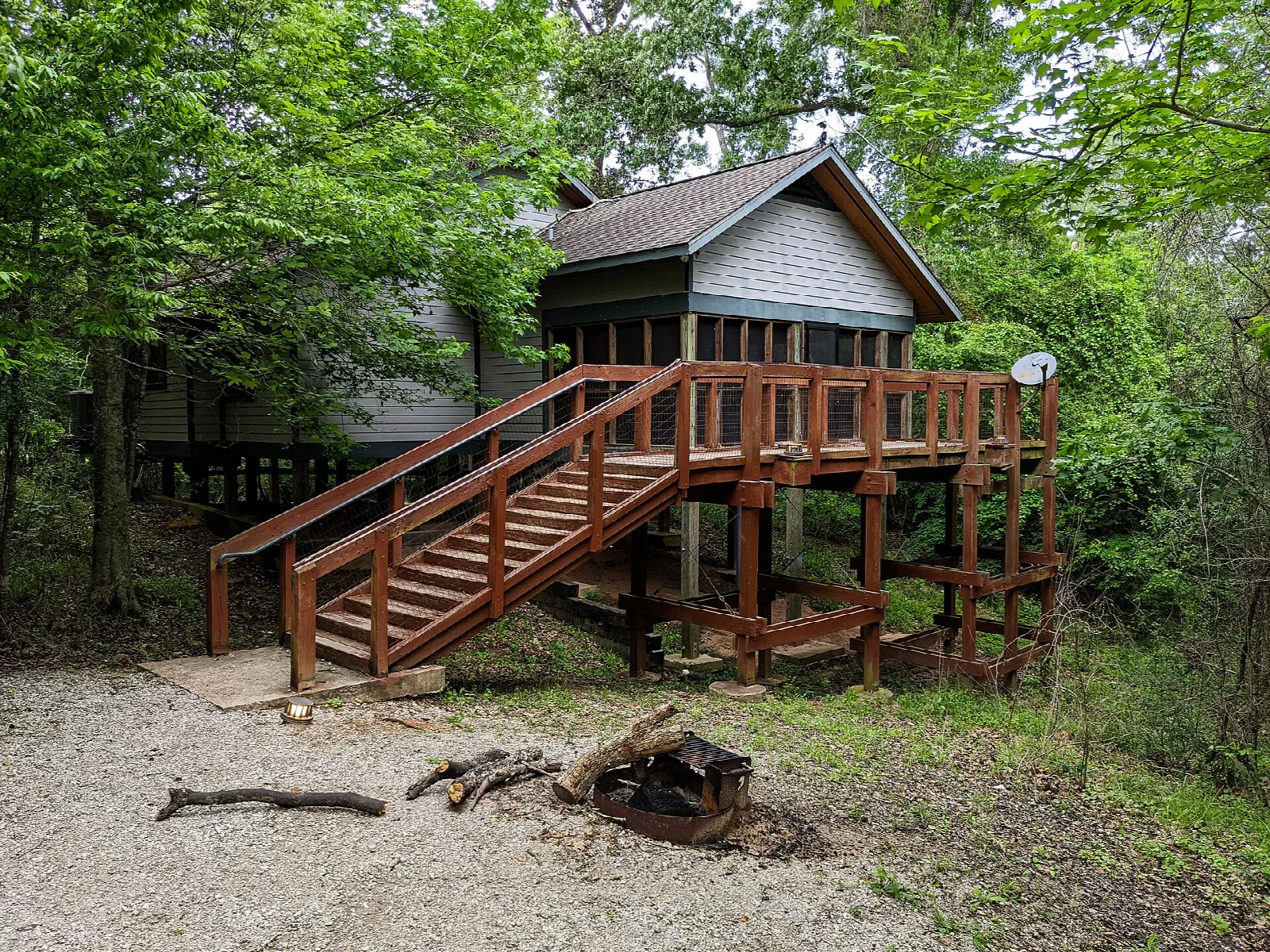 Wooden cabin raised on stairs in the woods beside a fire ring