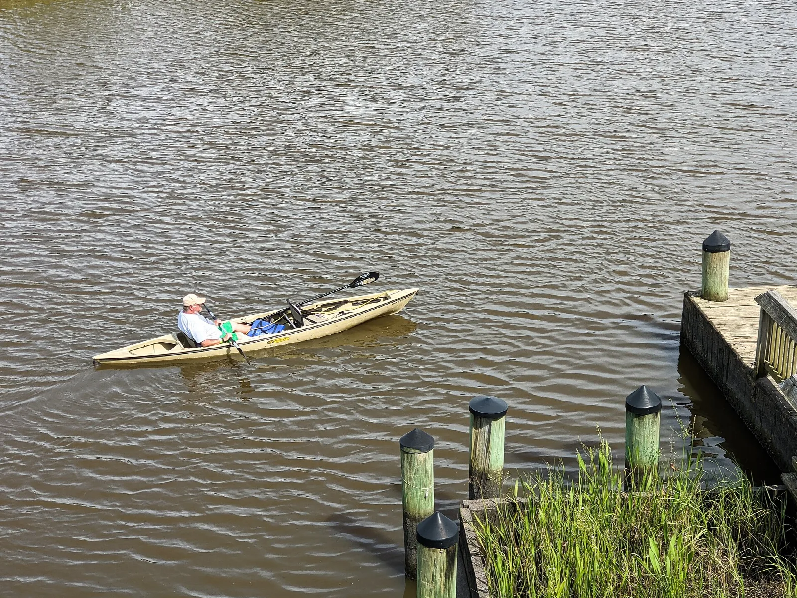 Person paddling a kayak on brown water beside a dock