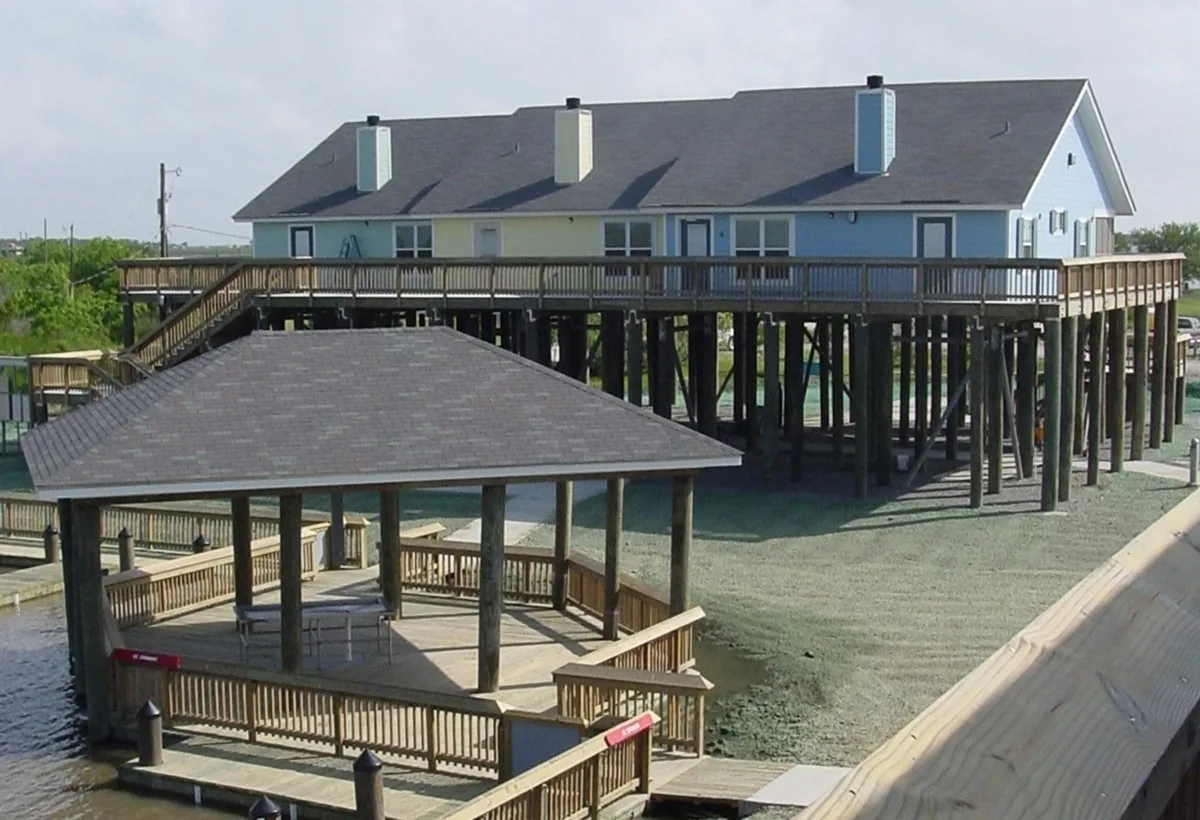 Light-blue raised cabin beside a covered wooden pavilion over the water