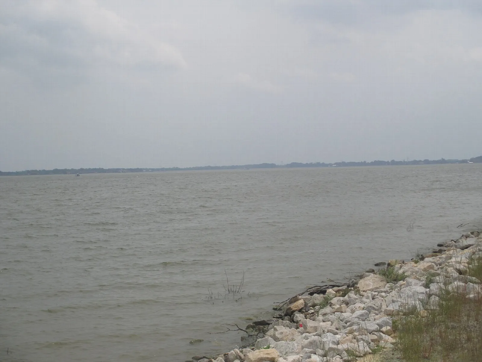 Wide open lake with a rocky bank in the foreground and a flat far shore