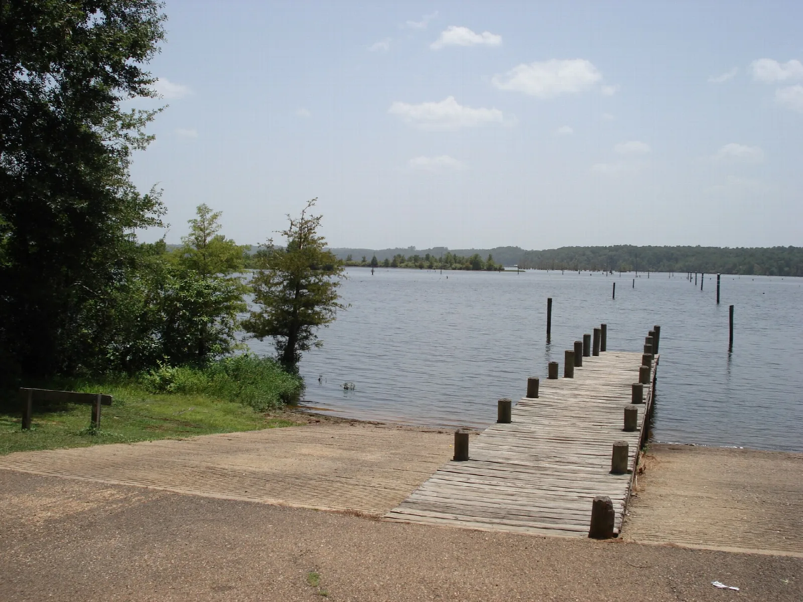 Wooden pier and boat ramp leading into a wide lake under a blue sky
