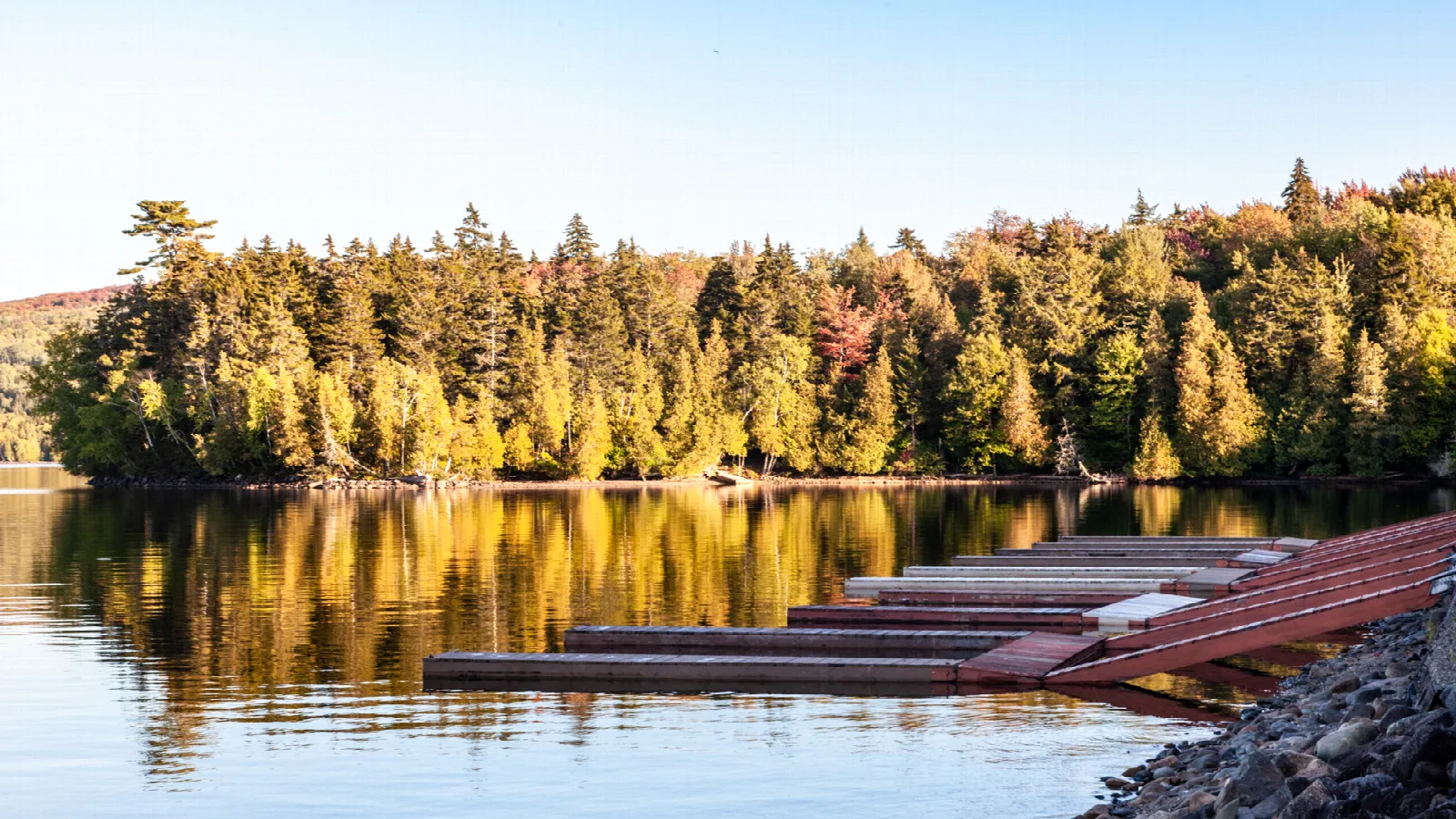 Wooden docks beside calm water with autumn trees reflected in the lake