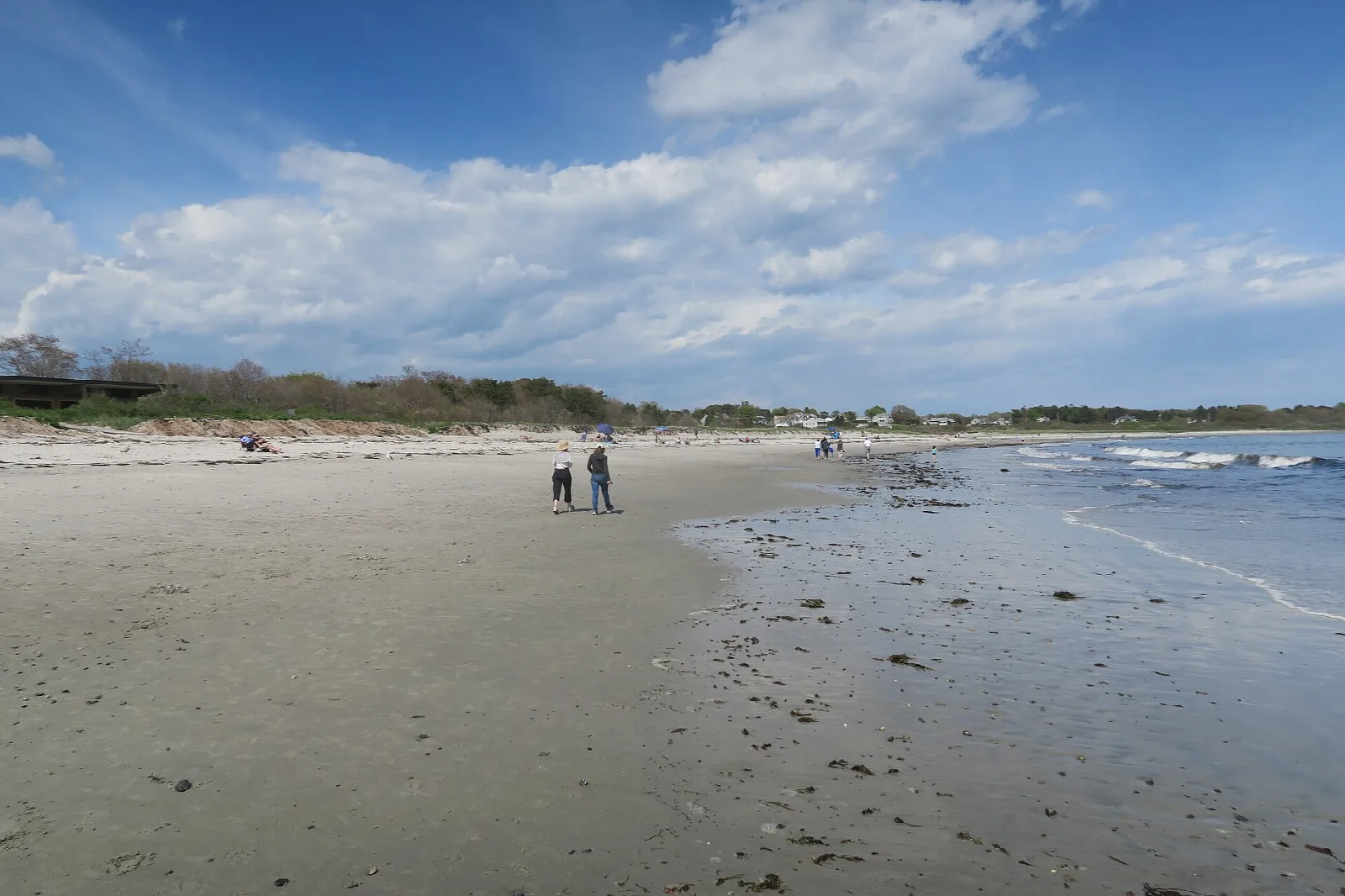 Wide sandy beach with a few walkers, surf on the right and dune grass behind