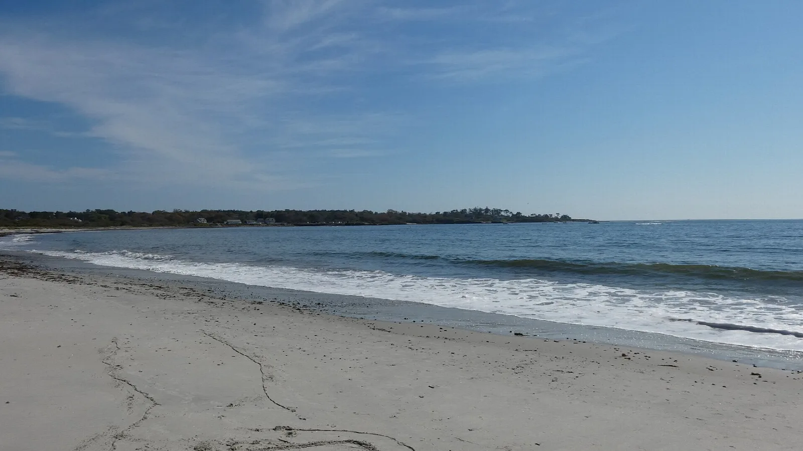 Gentle waves rolling onto a smooth sand beach under a pale blue sky