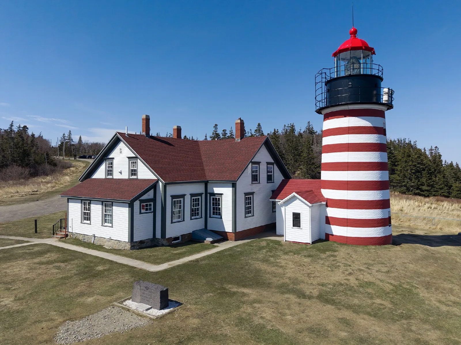 Striped lighthouse and keeper's house seen from above with evergreens behind