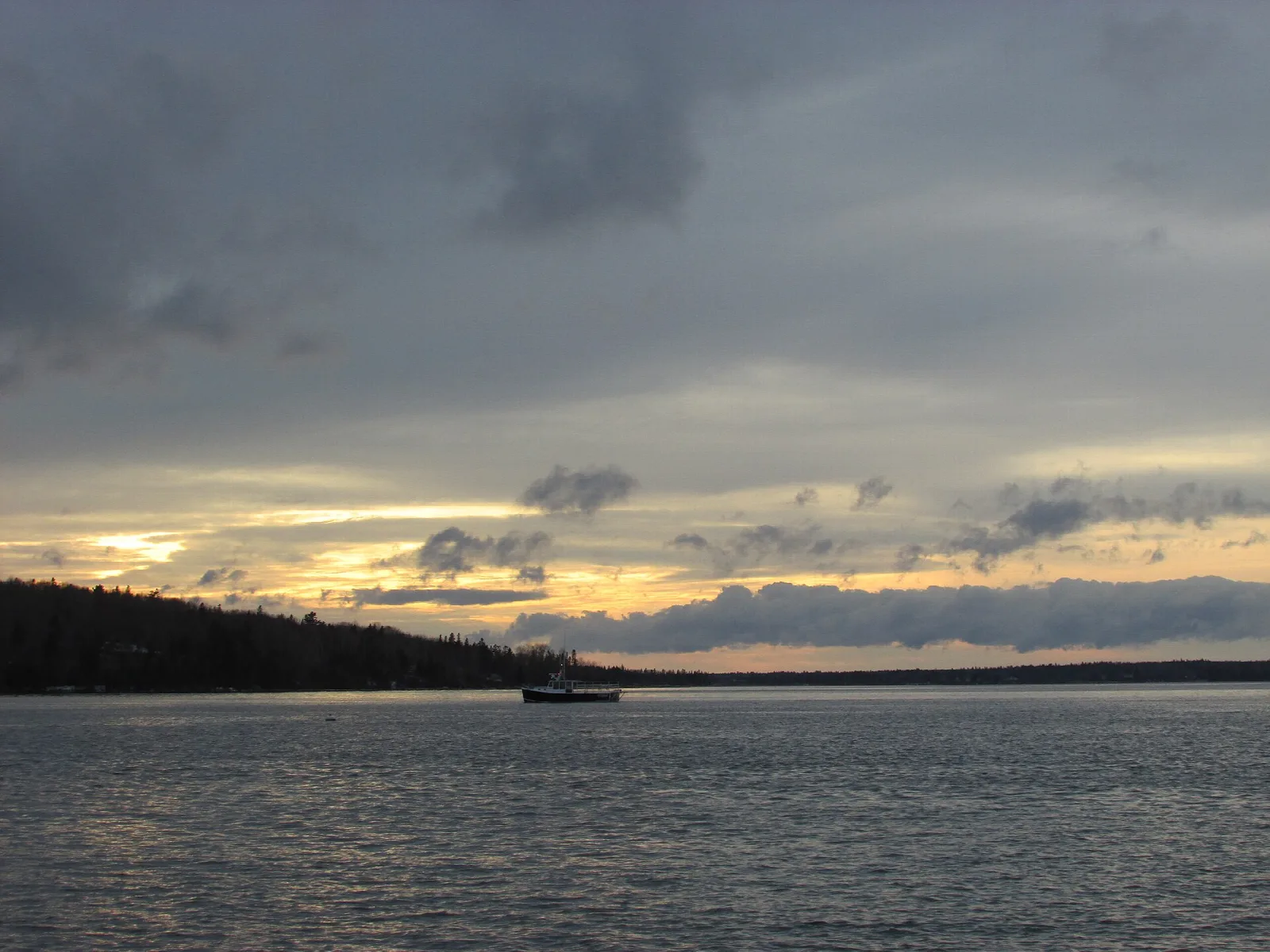 Wide bay at sunset under heavy clouds, a dark wooded point at left