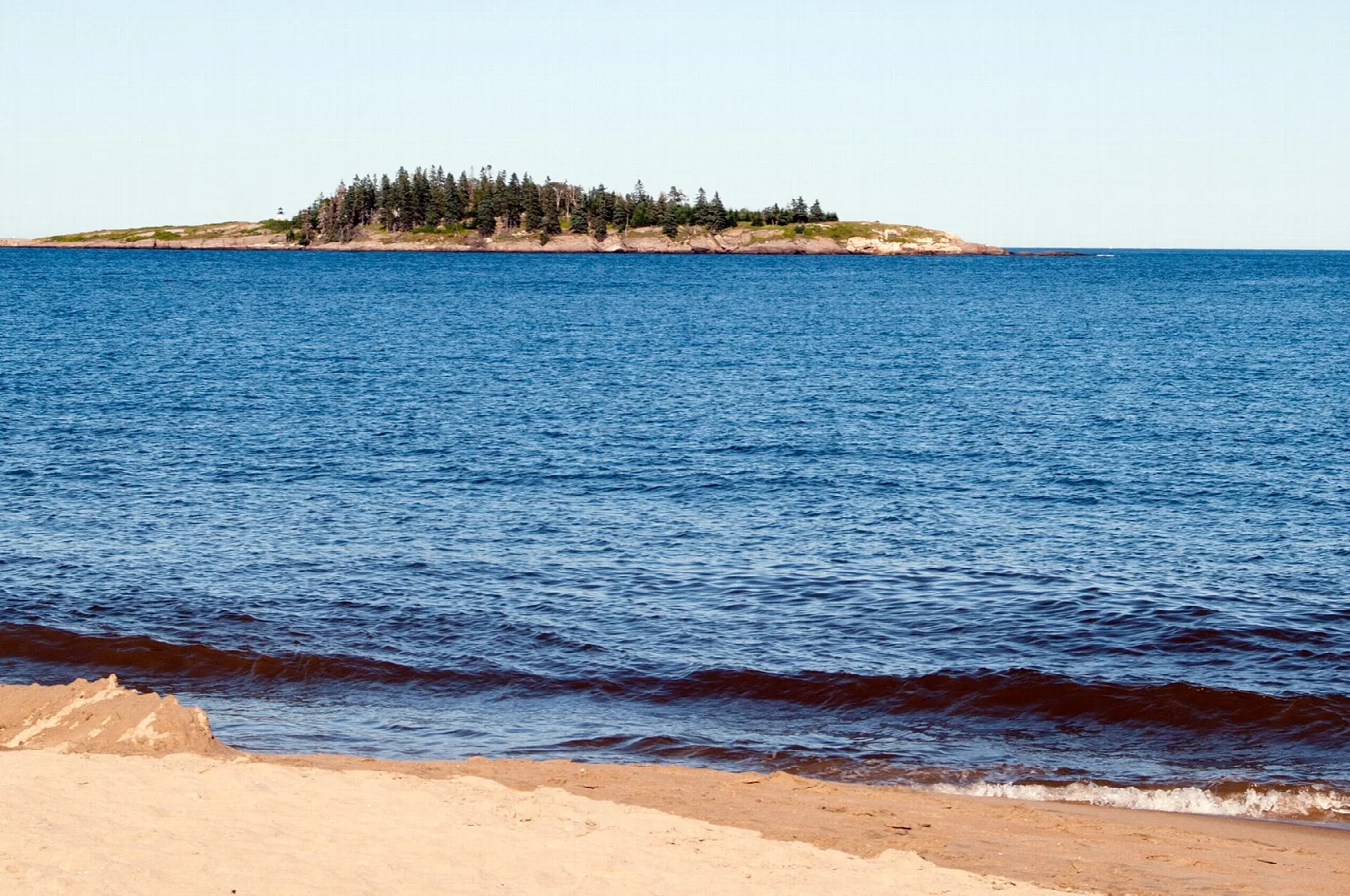 Blue ocean surf rolling onto sand with a small wooded island offshore