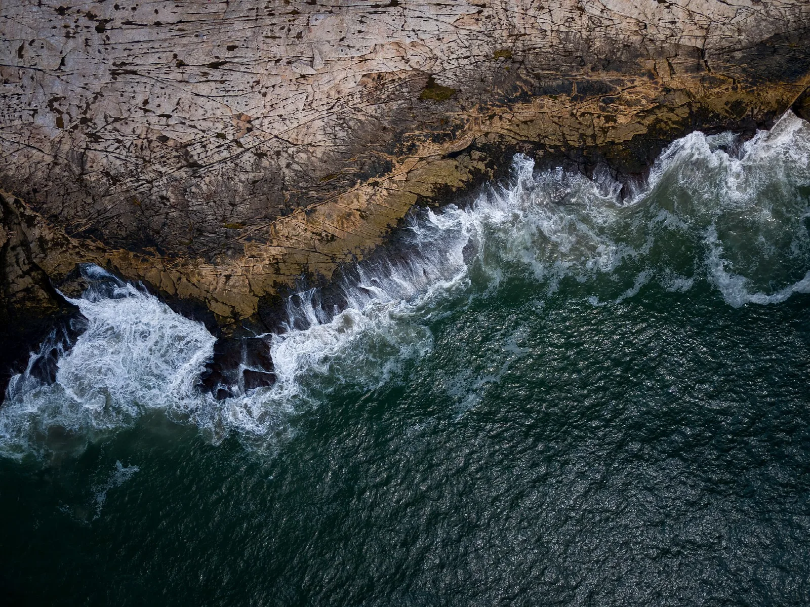 Aerial view of dark water breaking against a rocky shore