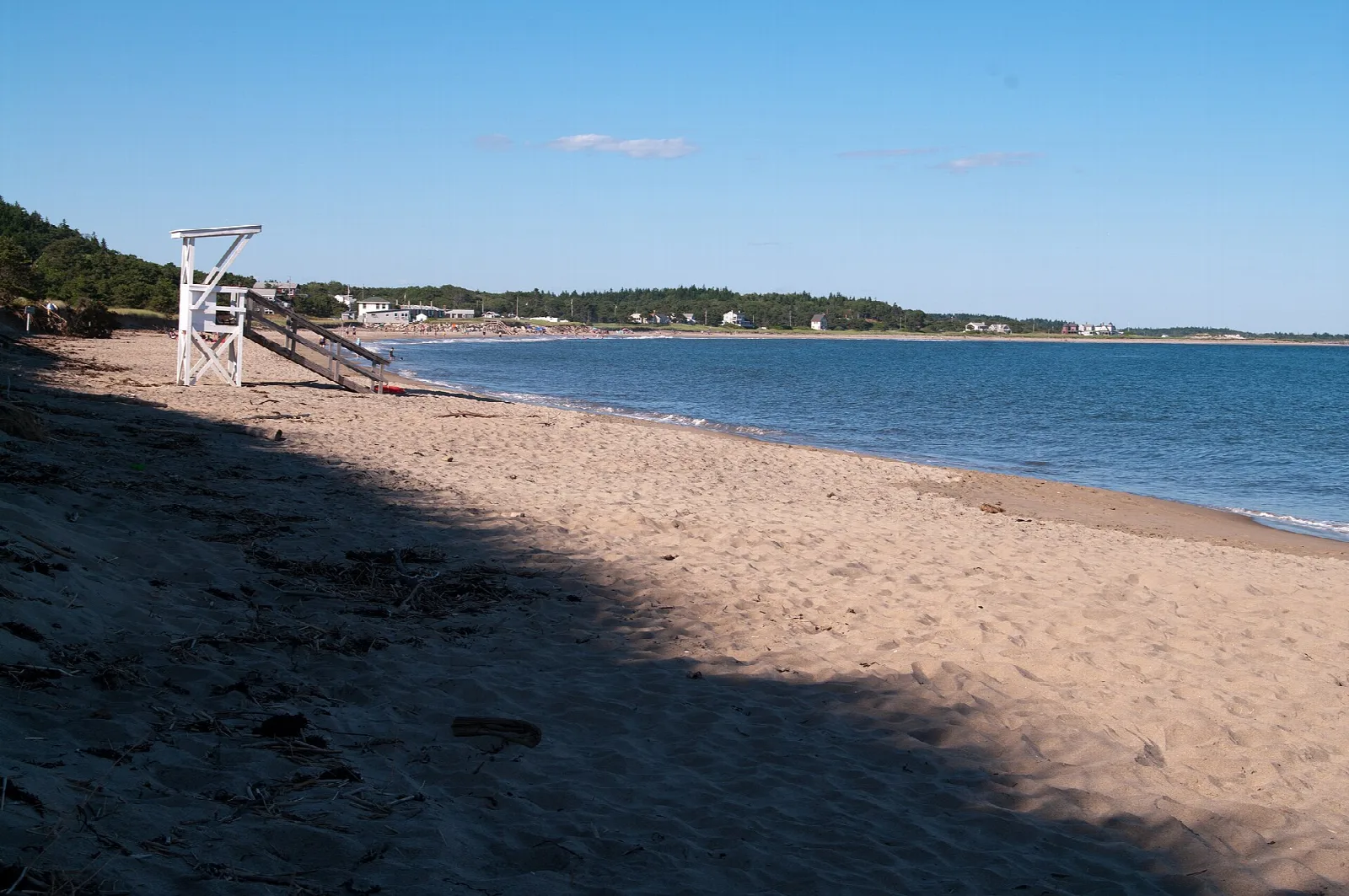 Sandy beach with a white lifeguard stand and blue water curving away to a distant shore