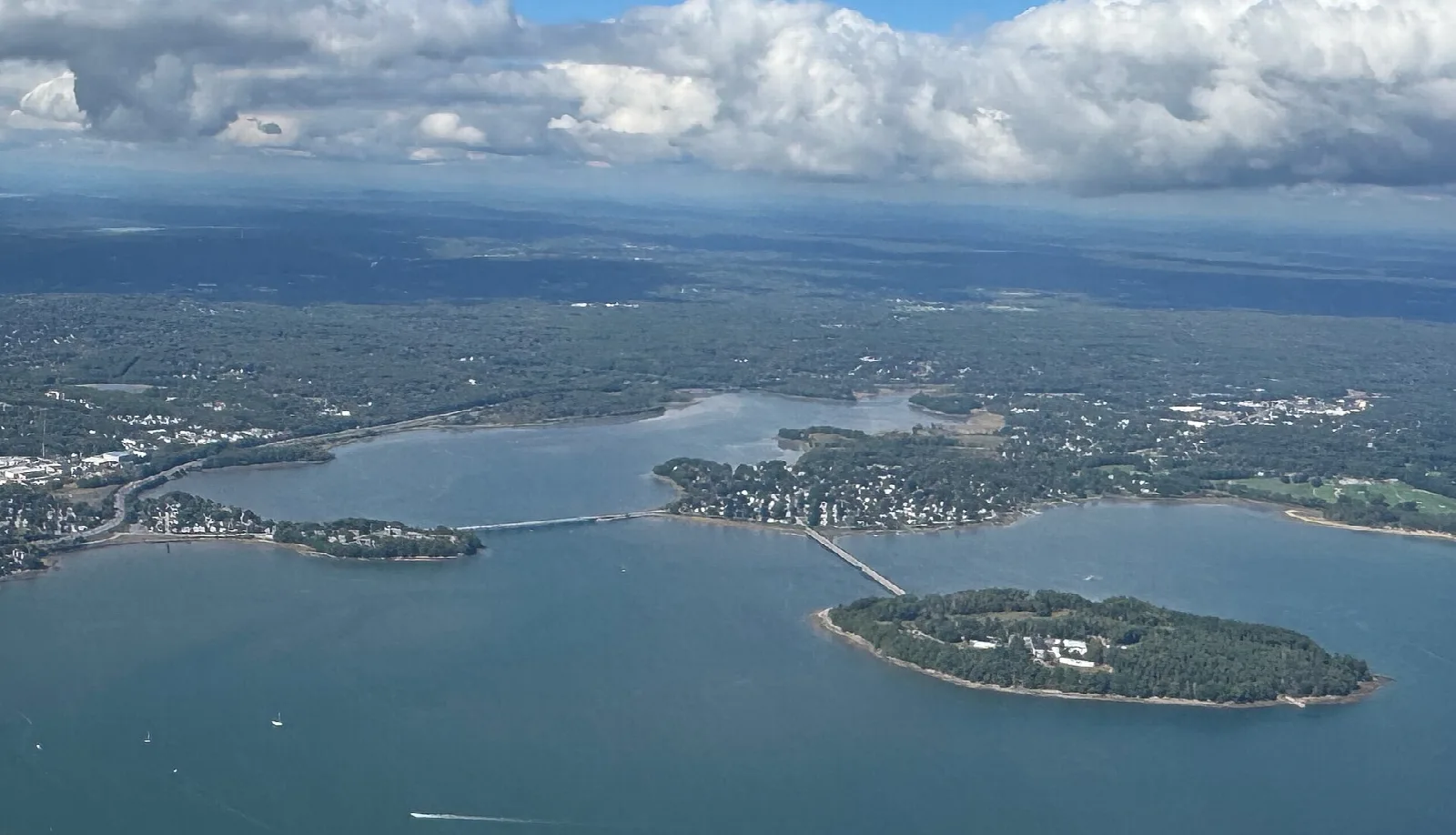 Aerial view of a wooded island joined to the mainland by a narrow causeway across blue water