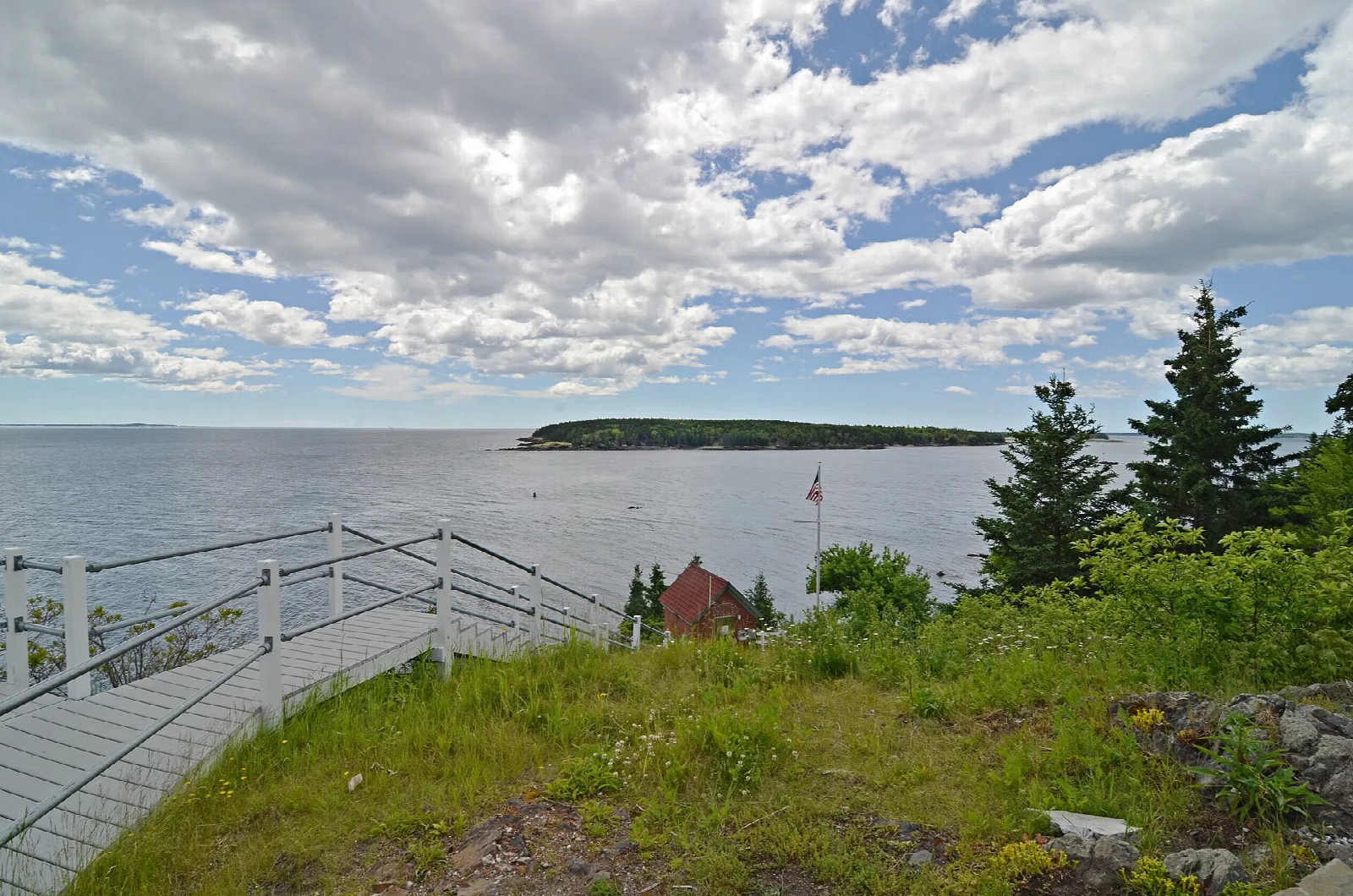 Wooden walkway with railings climbing a grassy hill toward the bay and an island