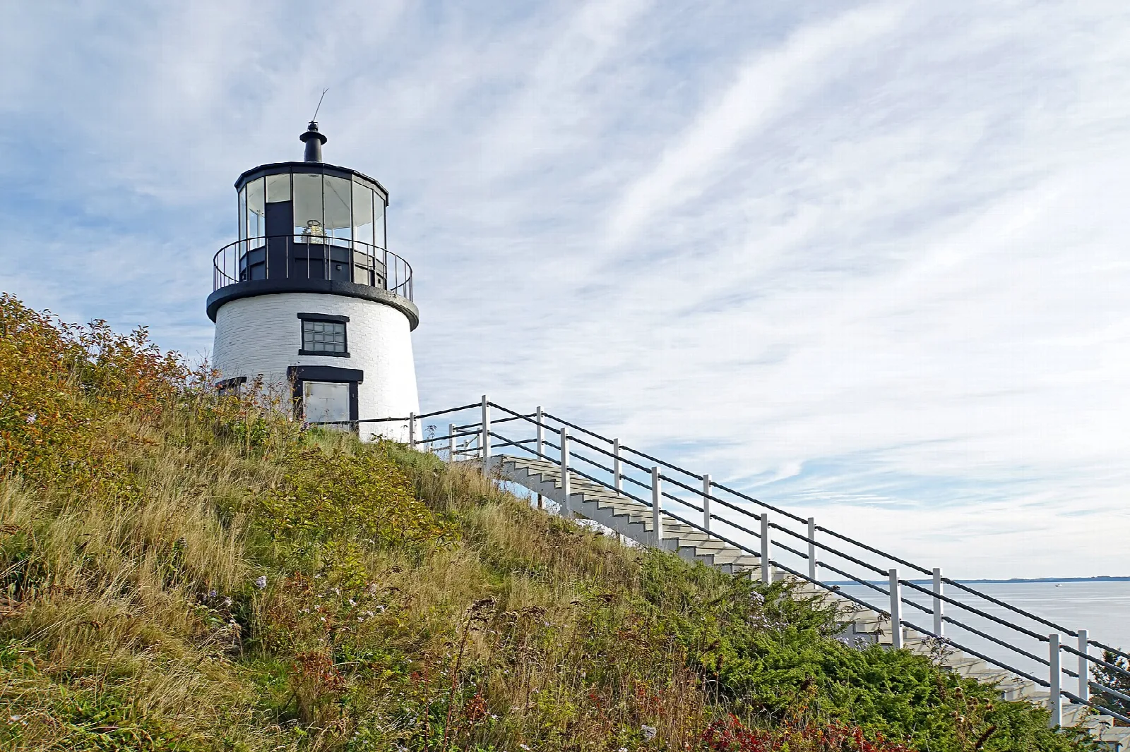Lighthouse at the top of a steep grassy slope with a long metal staircase