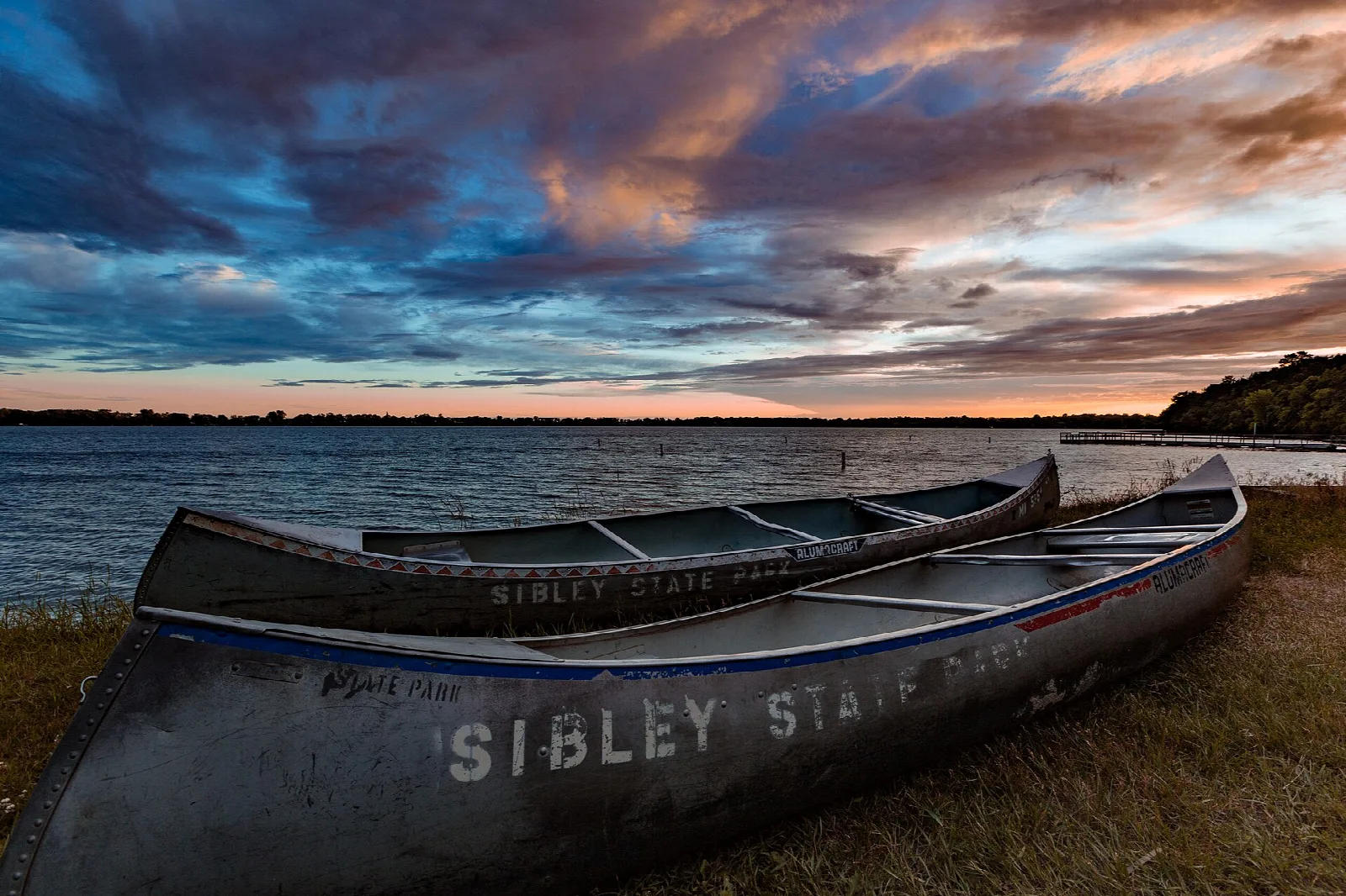 Two aluminum canoes marked Sibley State Park on a grassy shore at dusk