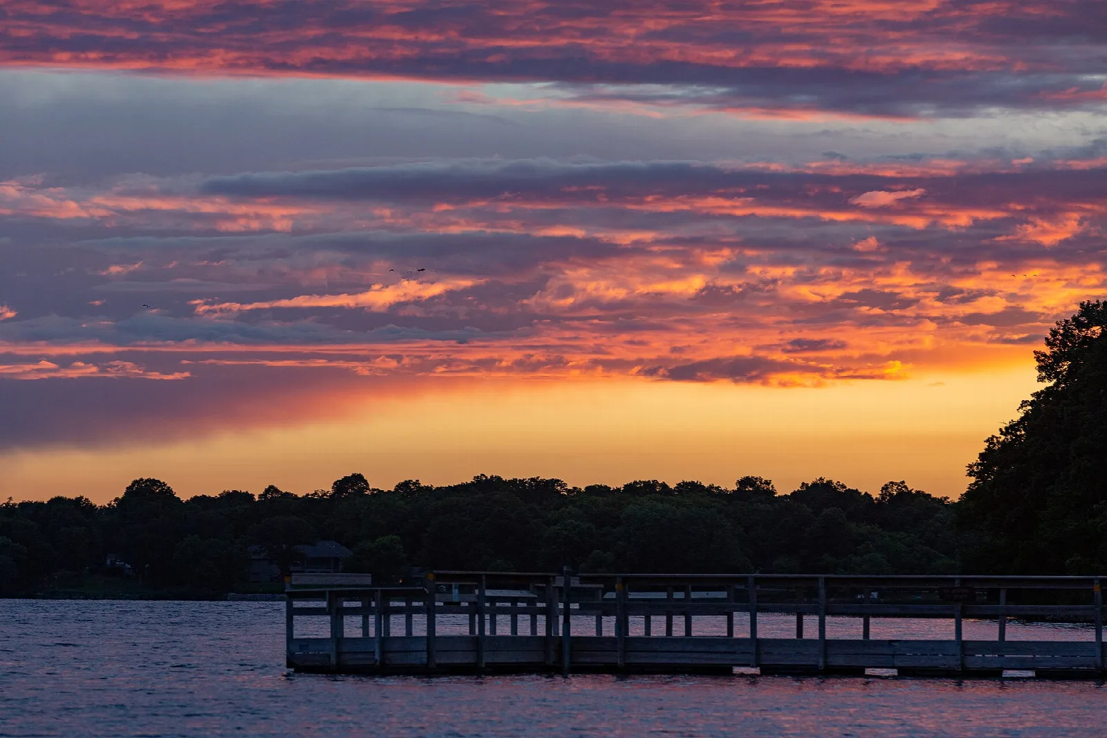 Wooden dock reaching into a lake under an orange and purple sunset sky