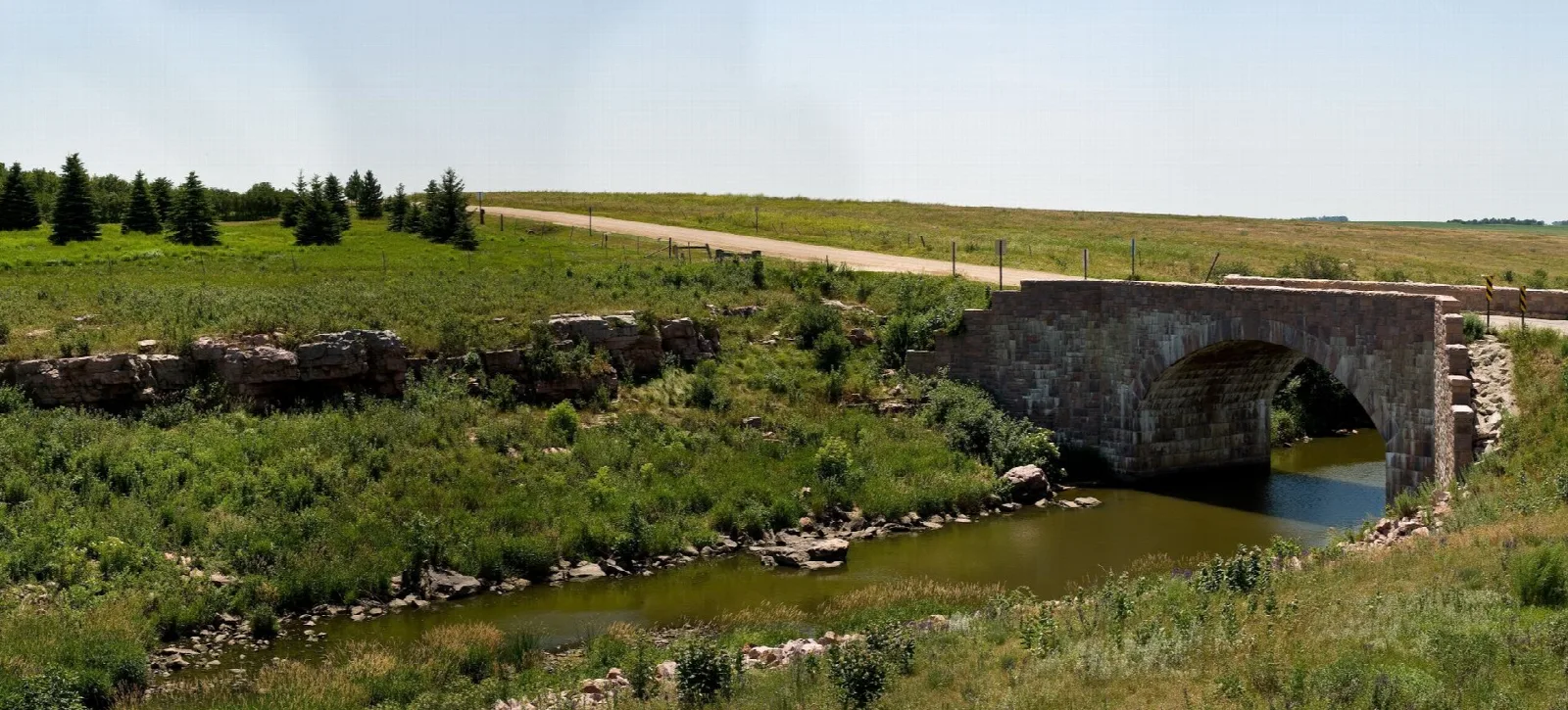 Old stone arch bridge over a small creek in open prairie