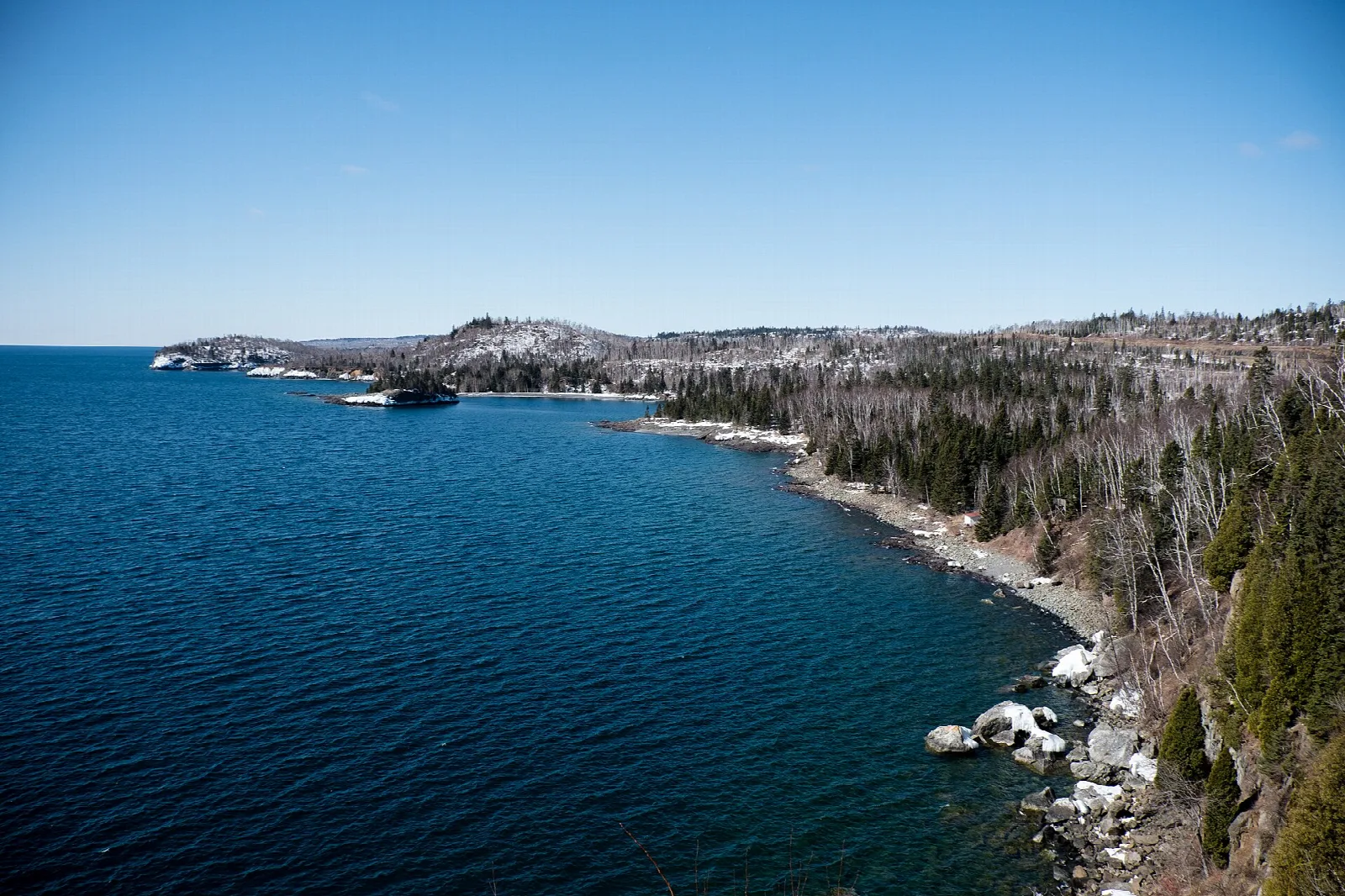 Deep blue Lake Superior and a forested rocky shoreline seen from above